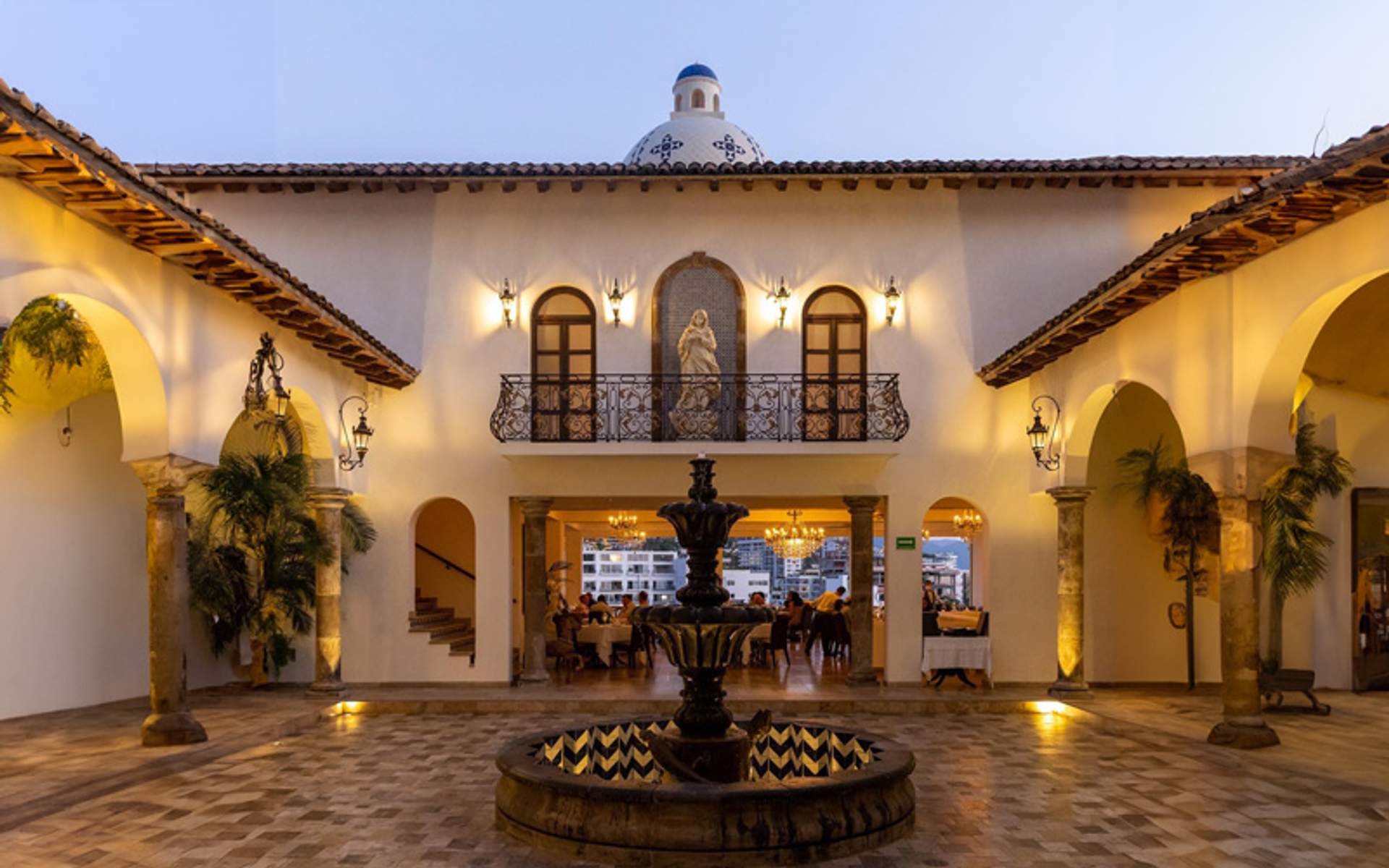An elegant courtyard with a central fountain, surrounded by arches and lit by warm evening lights, at La Iguana restaurant.