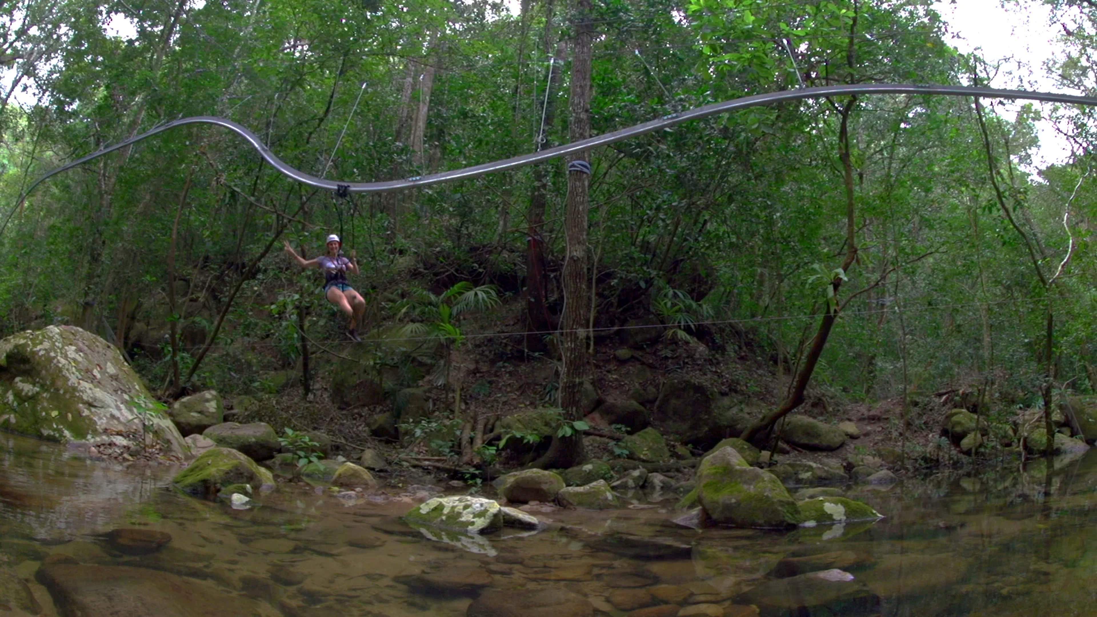 A person enjoys an extreme roller-coaster zipline over a rocky stream in a lush forest, showcasing adventure tourism in Puerto Vallarta.