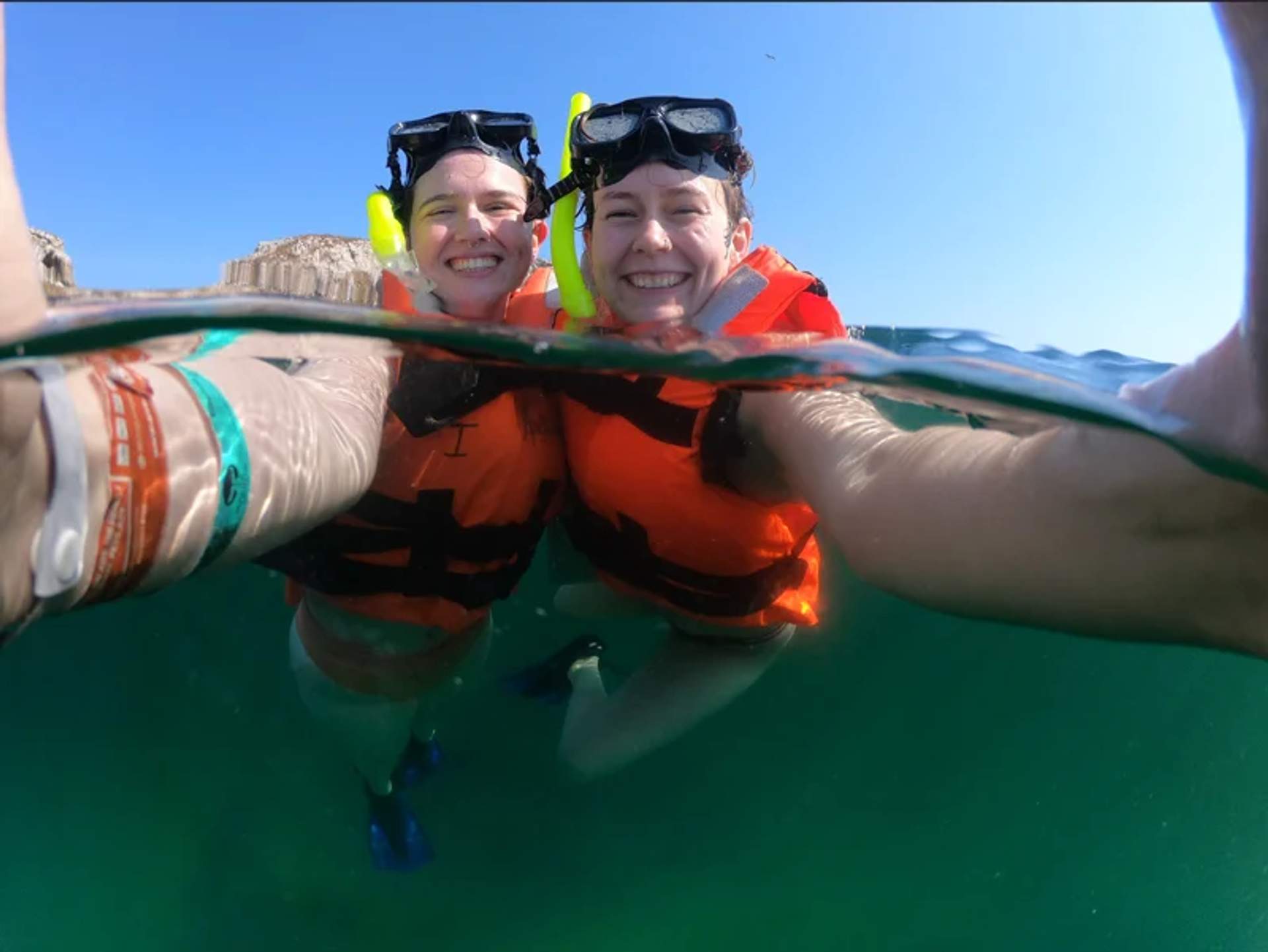 Two snorkelers smiling and taking a selfie in the clear waters of Marieta Islands, wearing life jackets and snorkel gear.