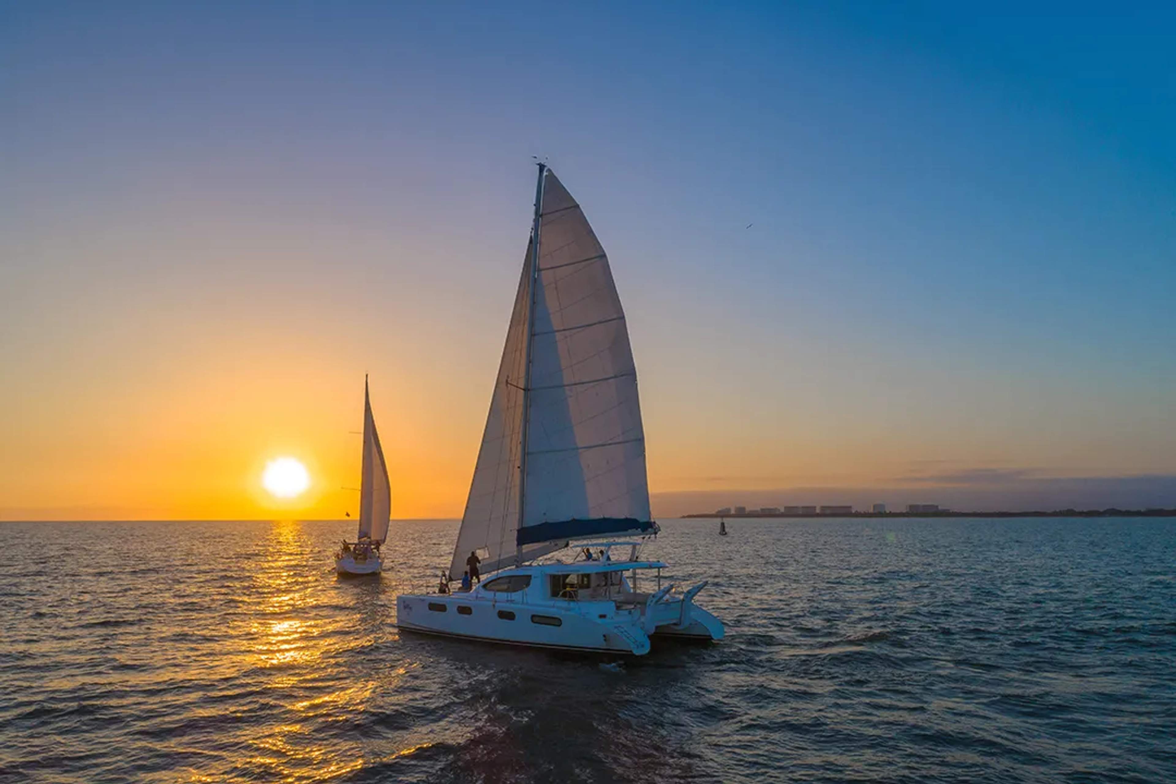 Sailboats on the ocean at sunset with a city skyline in the distance in Puerto Vallarta