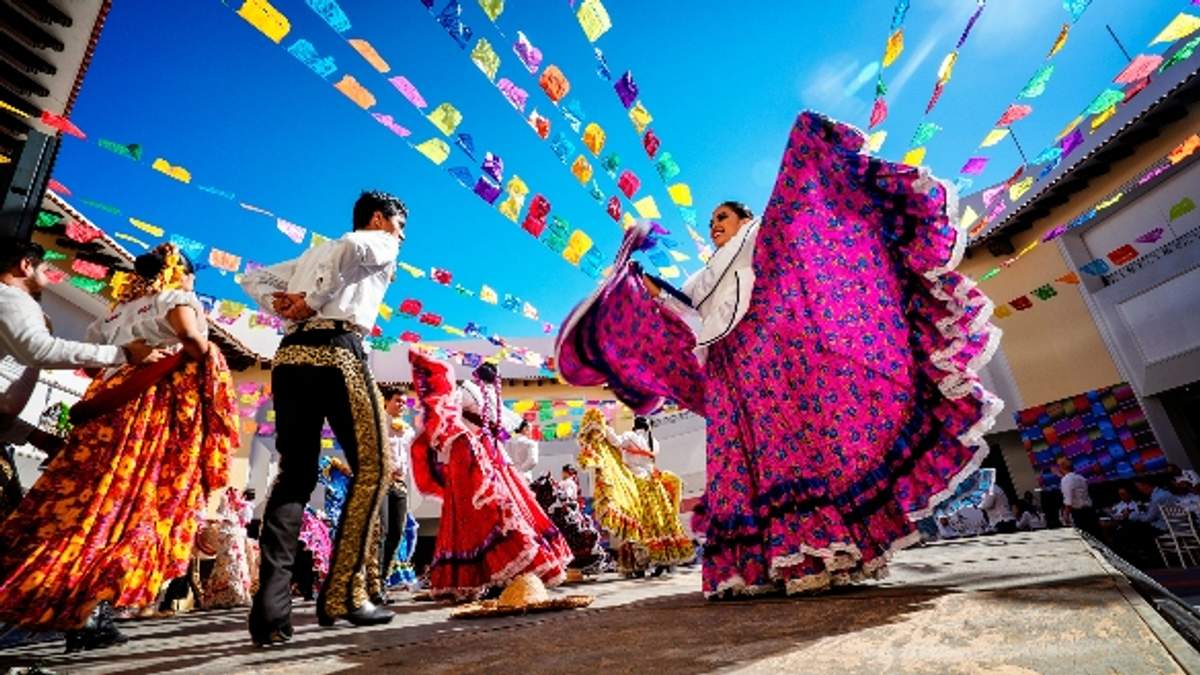 Bailarines con trajes tradicionales mexicanos actúan bajo coloridas banderitas durante una celebración festiva.
