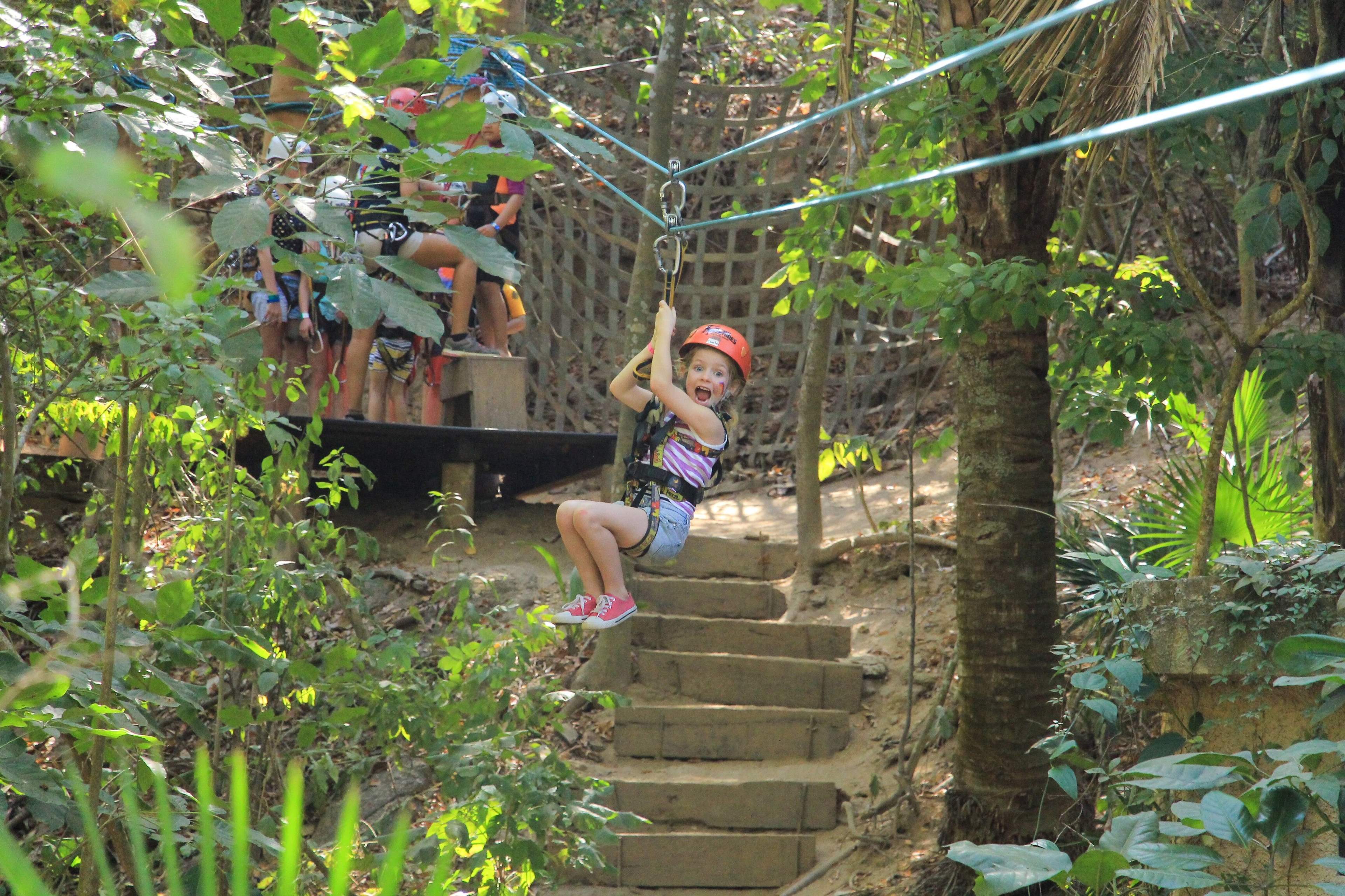 A young child excitedly ziplining through a forest, capturing the joy and thrill of a kid-friendly adventure.