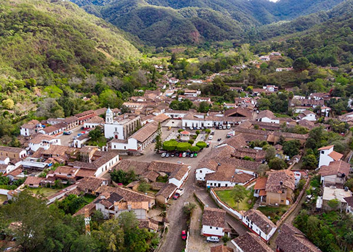 Vista aérea de San Sebastián del Oeste, un pequeño pueblo con techos de tejas rojas enclavado en un valle montañoso y frondoso.