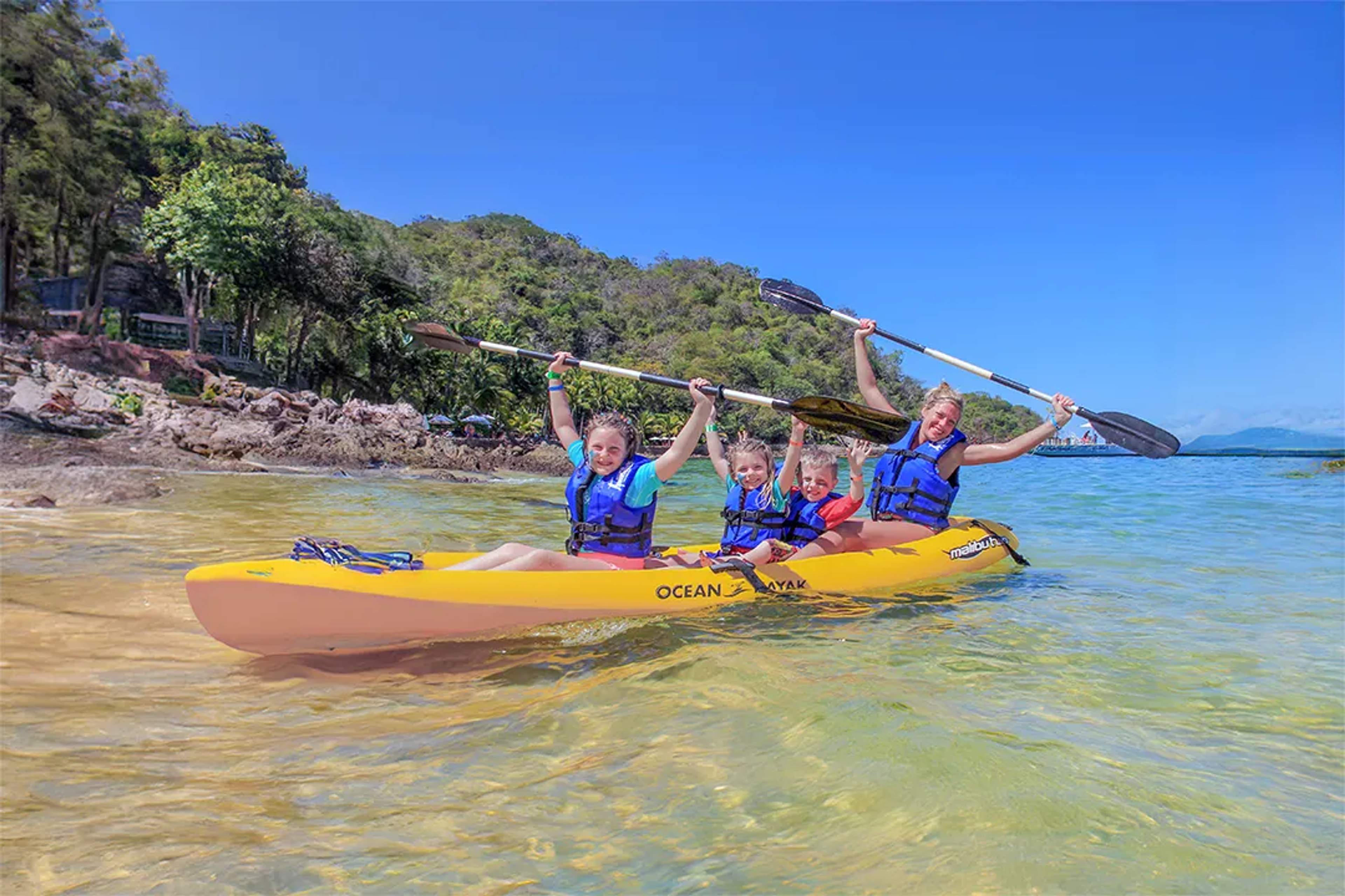 Family kayaking in shallow water near a tropical shoreline in Las Caletas