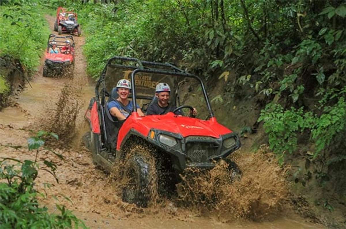 Turistas conduciendo ATVs rojos por un sendero de jungla embarrado durante una aventura todoterreno en Puerto Vallarta.