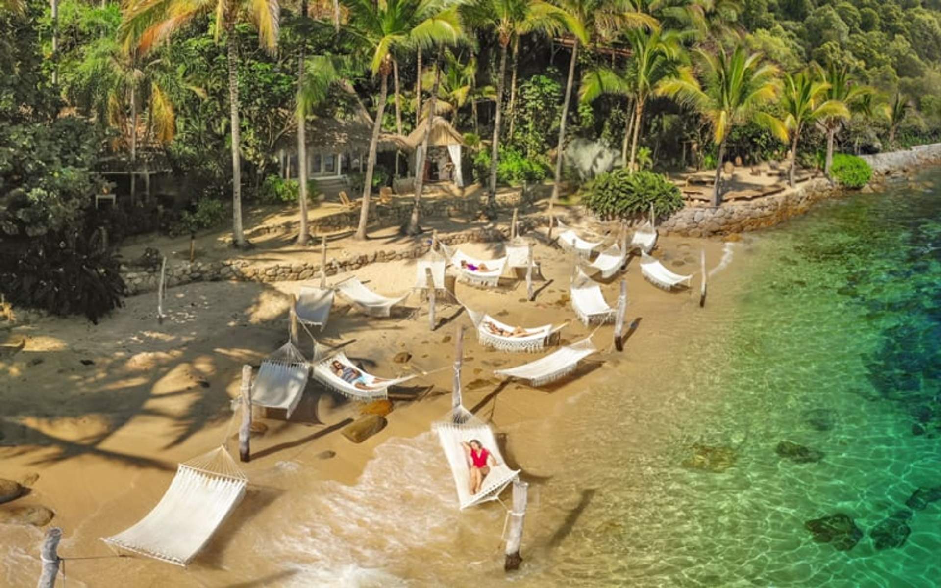 Hamacas en una playa de arena rodeada de palmeras y agua turquesa clara en Las Caletas, Puerto Vallarta.