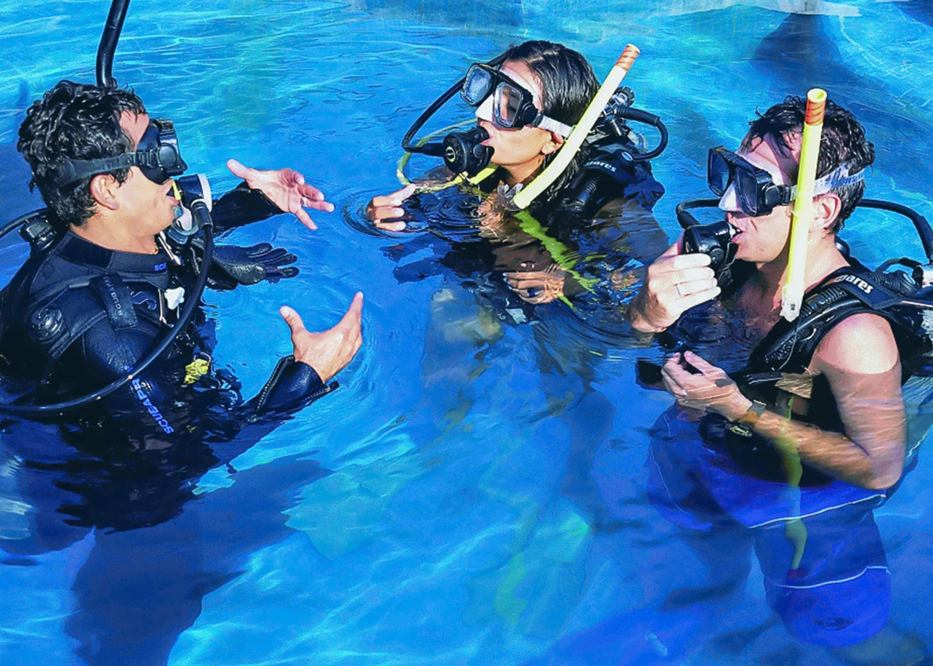 A scuba instructor teaching two students how to use diving equipment in a pool during a scuba diving class.