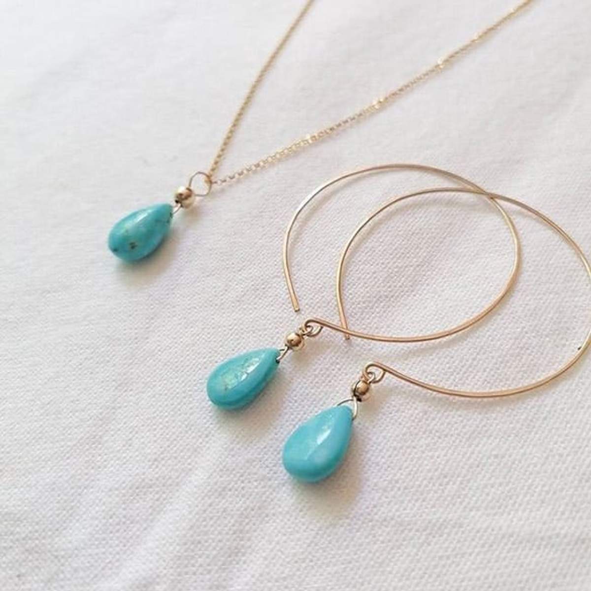 Aretes de aro de oro y un collar con colgantes en forma de lágrima turquesa sobre un fondo de tela blanca.