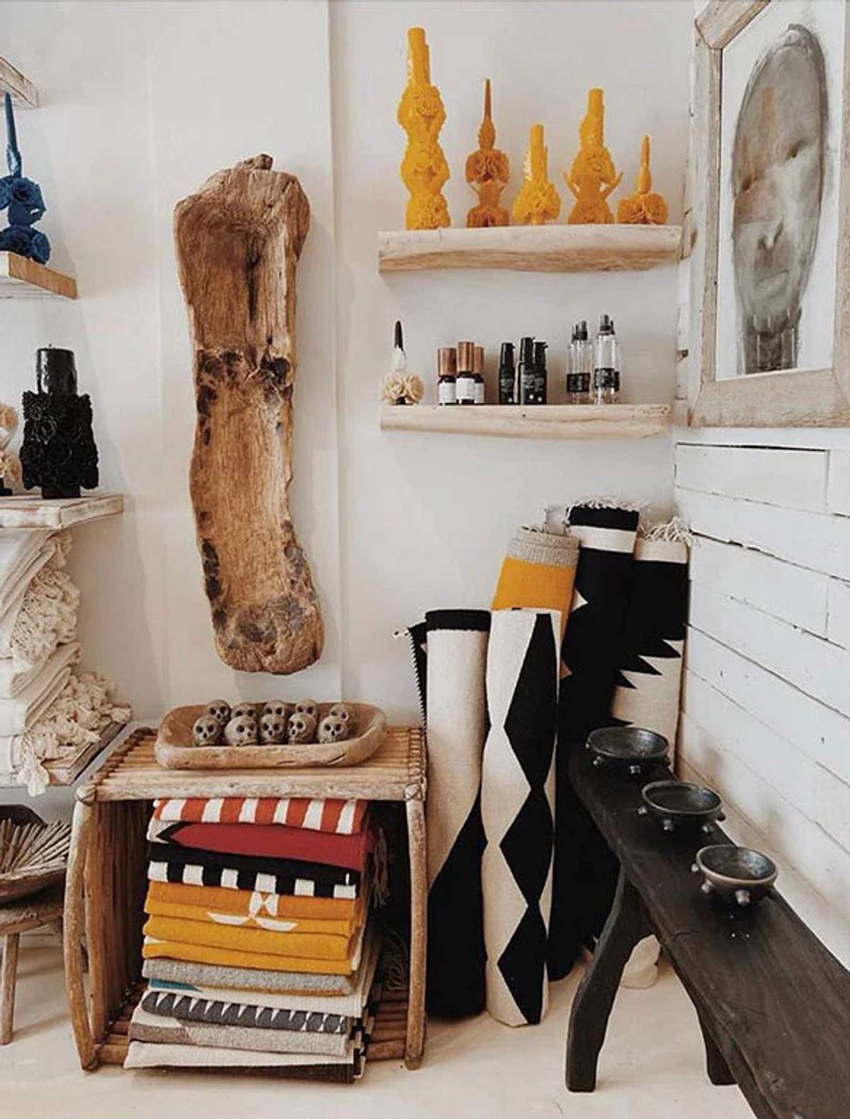 Exhibición en boutique con mantas dobladas, alfombras enrolladas, artículos decorativos y acentos de madera en estantes y mesas.