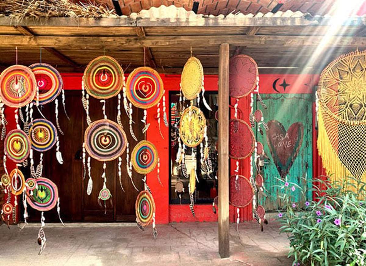 Atrapasueños coloridos colgando fuera de una tienda con fachada roja vibrante, bajo un techo de madera, con flores al lado.