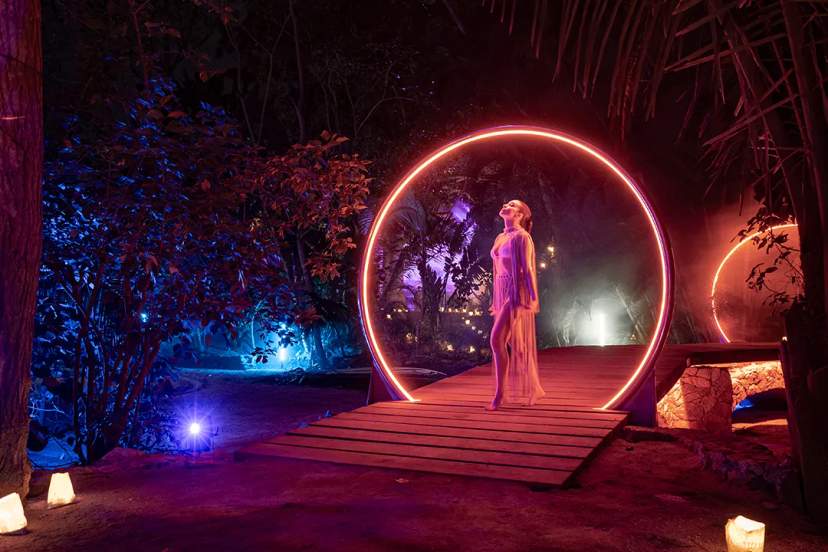 Mujer en un anillo brillante en la noche, rodeada de árboles iluminados de colores en Puerto Vallarta