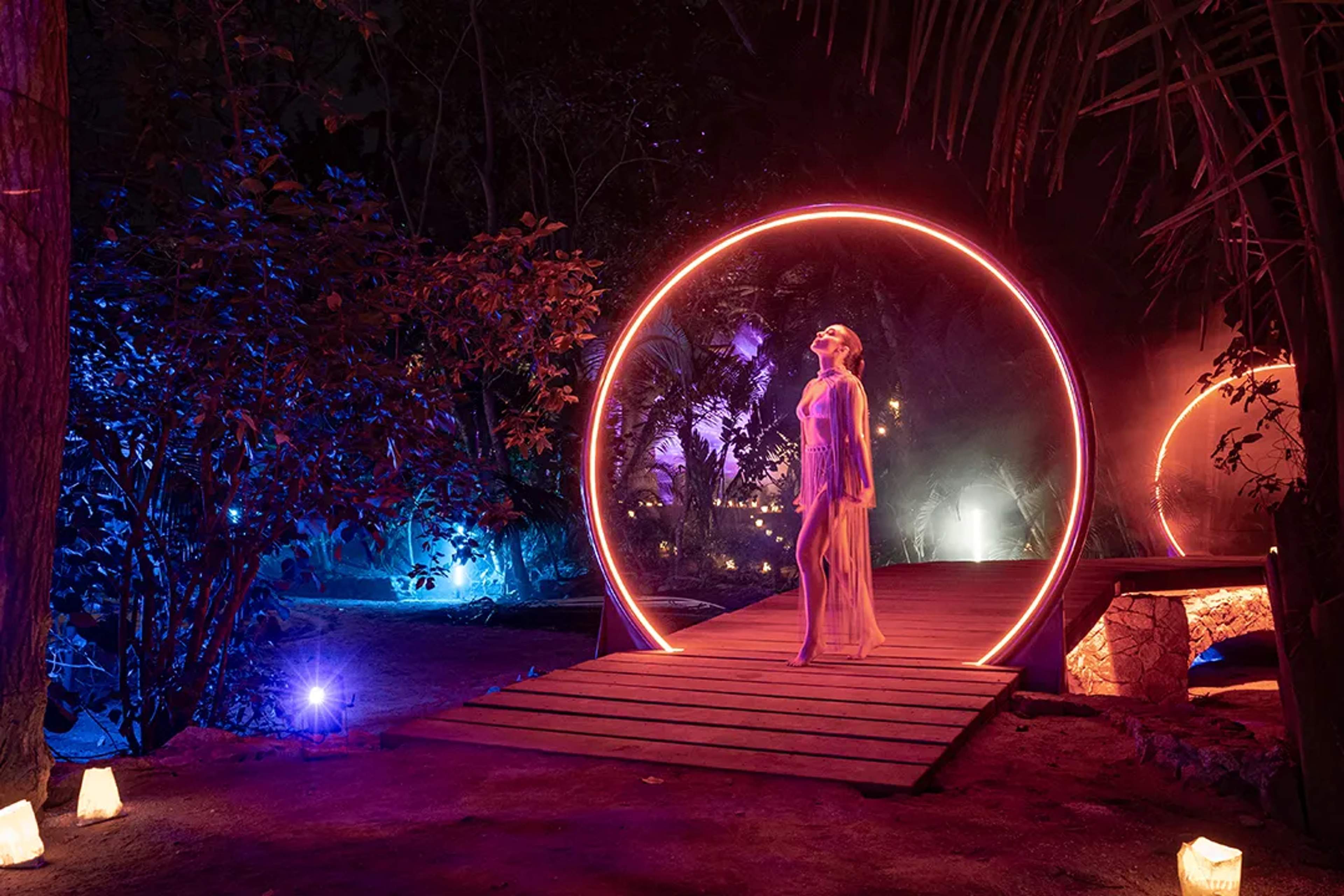 Woman stands in a glowing ring at night surrounded by colorful illuminated trees in Puerto Vallarta, creating a magical scene