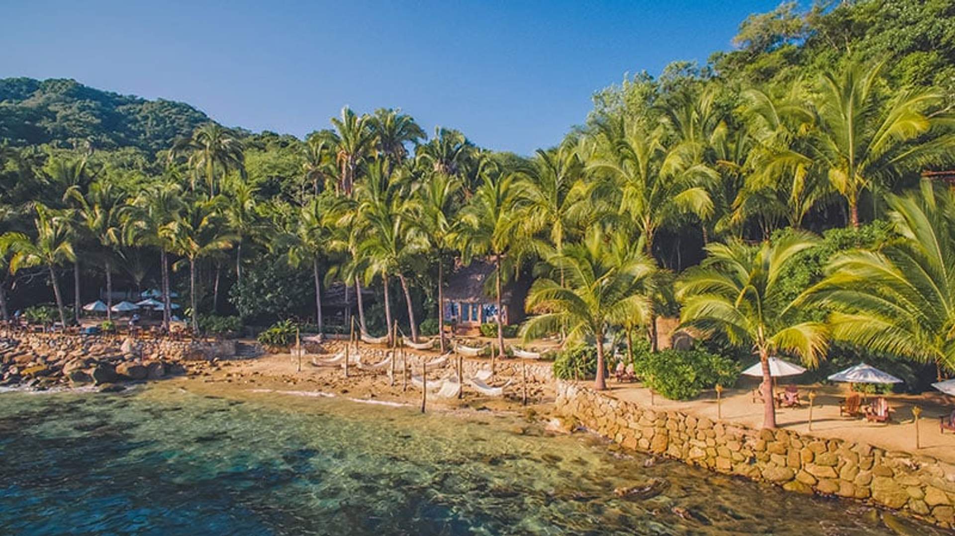 Una zona tropical frente a la playa en Puerto Vallarta con palmeras, hamacas y agua azul clara.