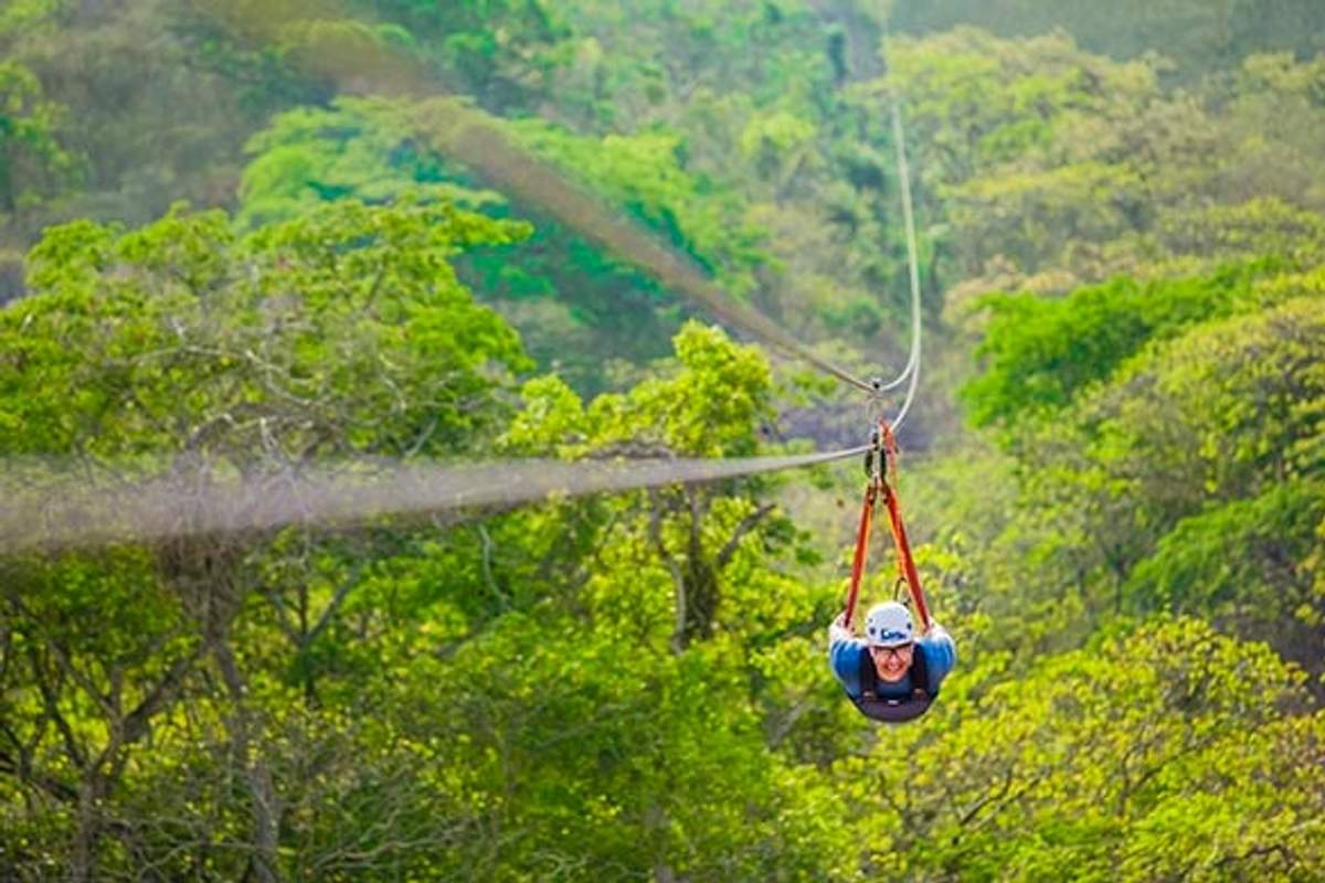 Persona haciendo tirolesa en posición de Superman sobre un exuberante bosque verde en Puerto Vallarta, disfrutando de una aventura emocionante.