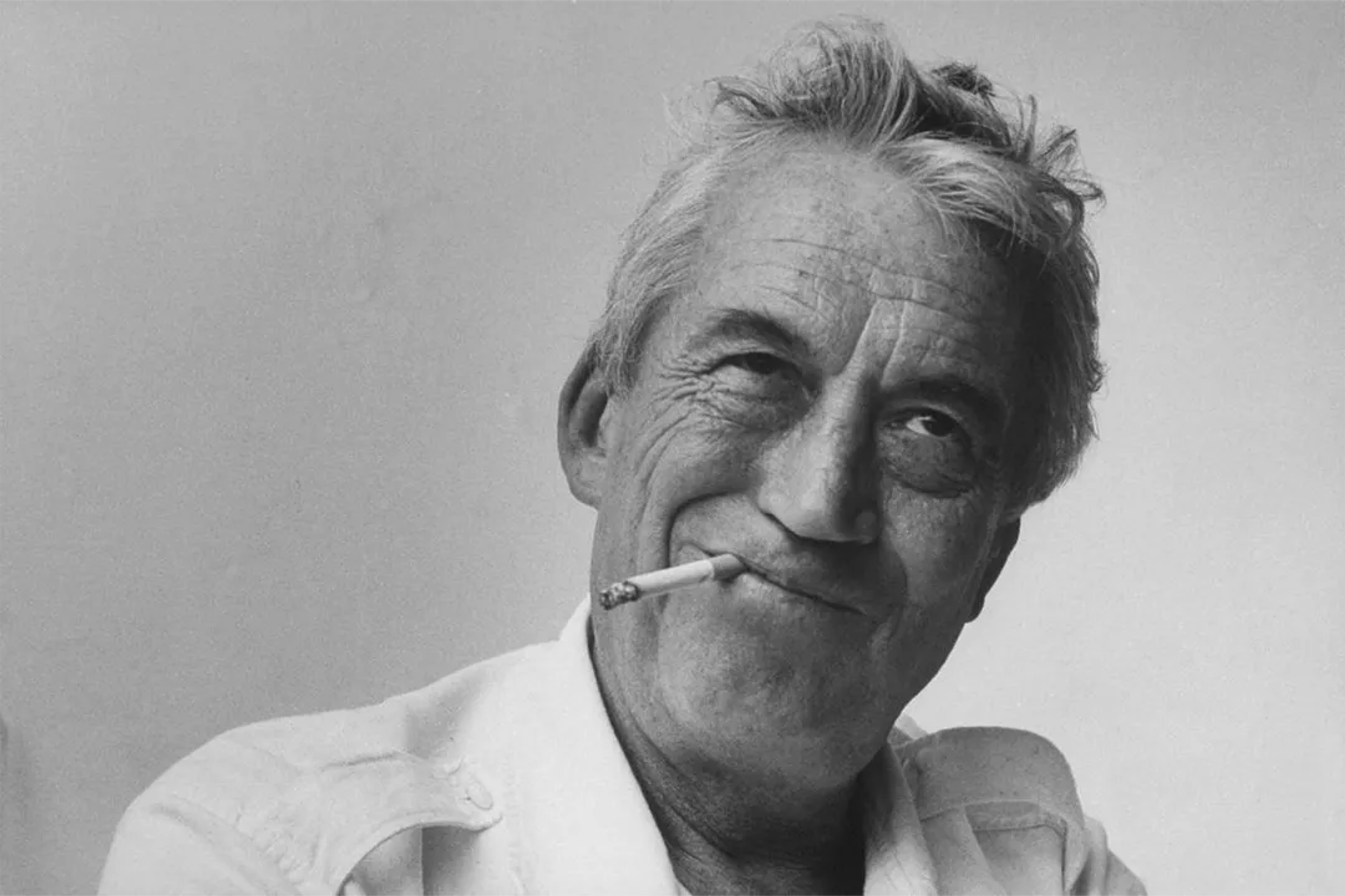 John Huston, smiling with a cigarette, captures a candid moment of charm and rebellion.