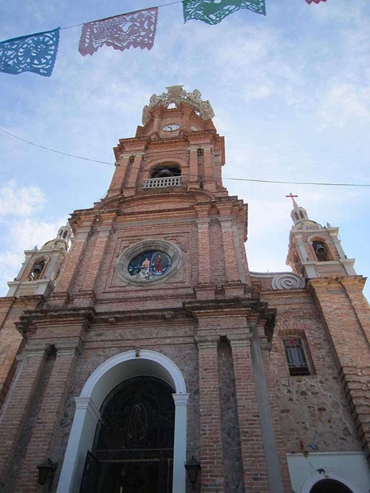 Vista en ángulo bajo de la Iglesia de Nuestra Señora de Guadalupe en Puerto Vallarta, con coloridas banderitas de papel picado arriba.