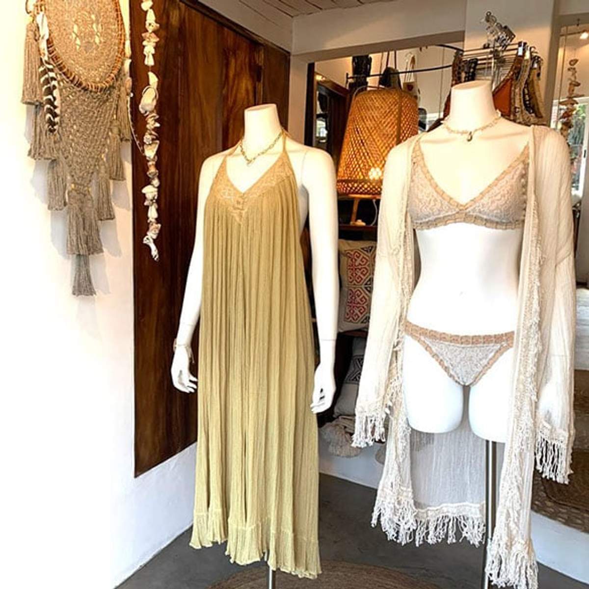 Dos maniquíes mostrando un vestido beige y un conjunto de lencería de encaje con cárdigan en una boutique.