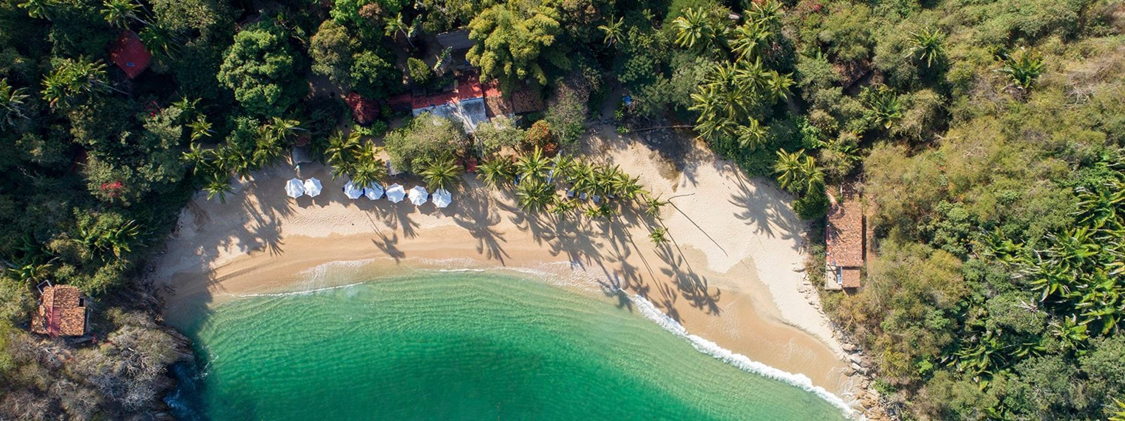 An aerial view of Marieta Hidden Beach, showcasing a secluded beach with golden sand, clear turquoise water, and dense tropical vegetation. Beach umbrellas and palm trees line the shore.