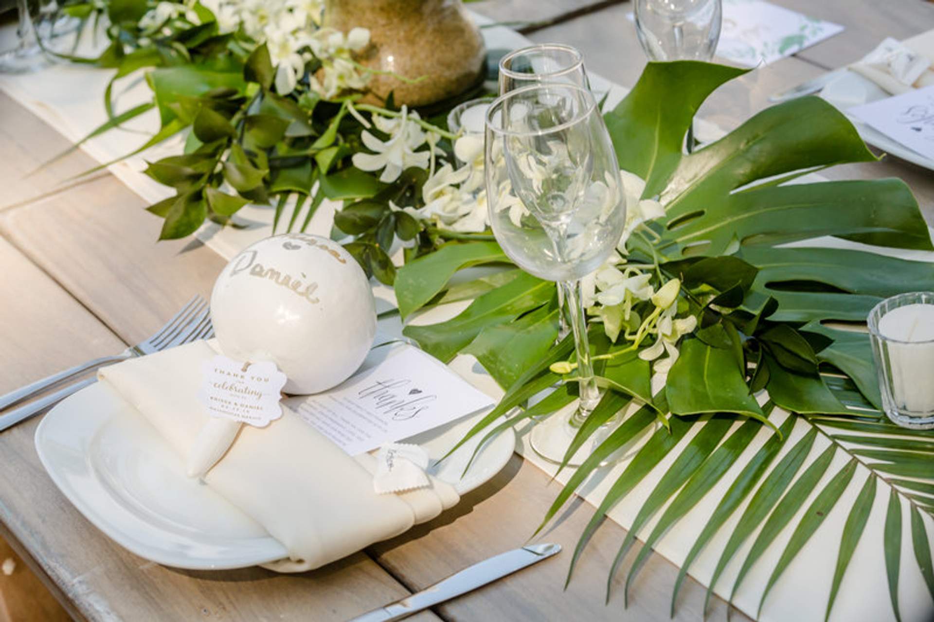 Elegante montaje de mesa de boda con hojas tropicales, decoración personalizada y cristalería, creando un ambiente exuberante y acogedor.