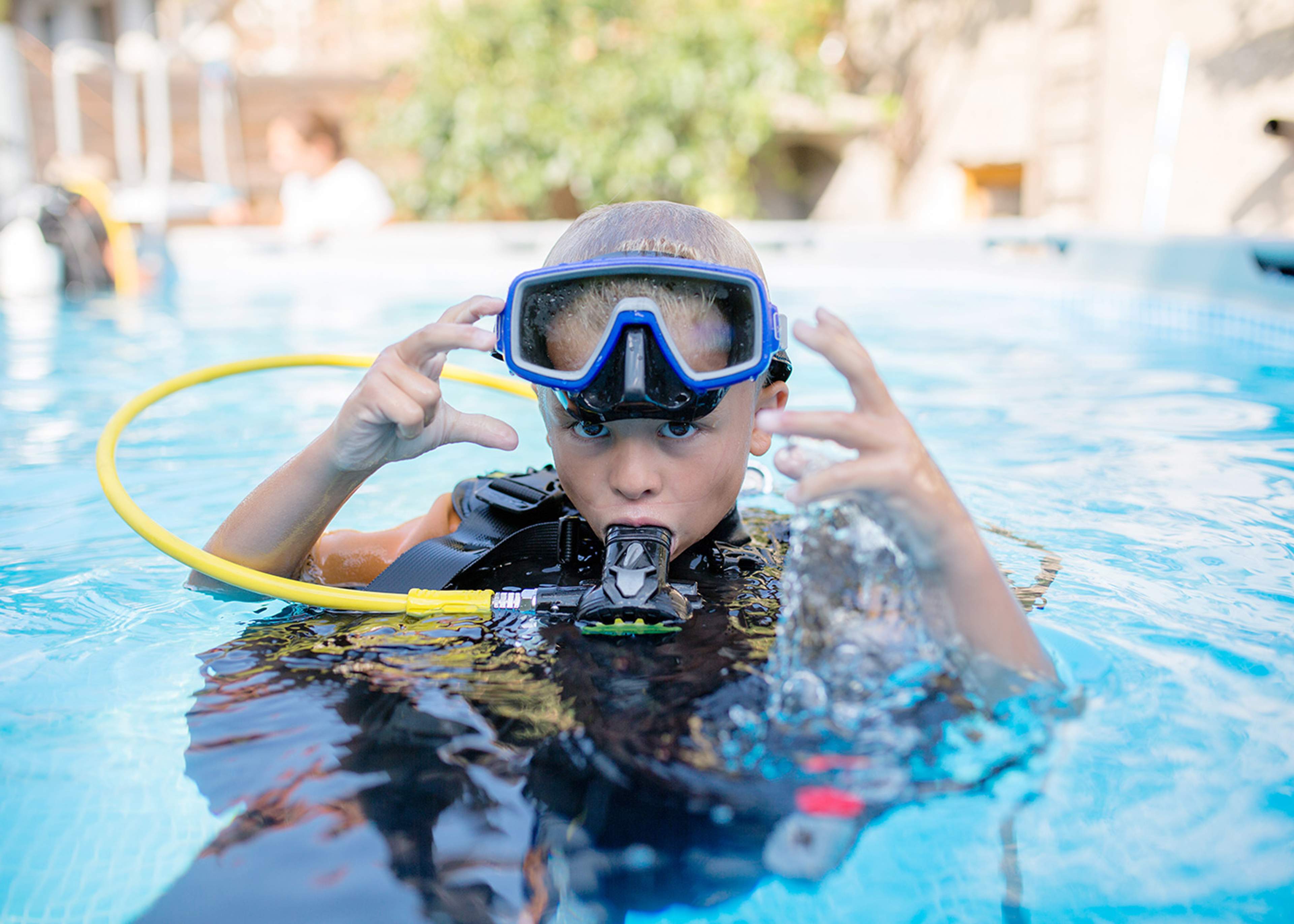 A child learning to scuba dive, wearing scuba gear and practicing in a pool during a kids' scuba diving class.