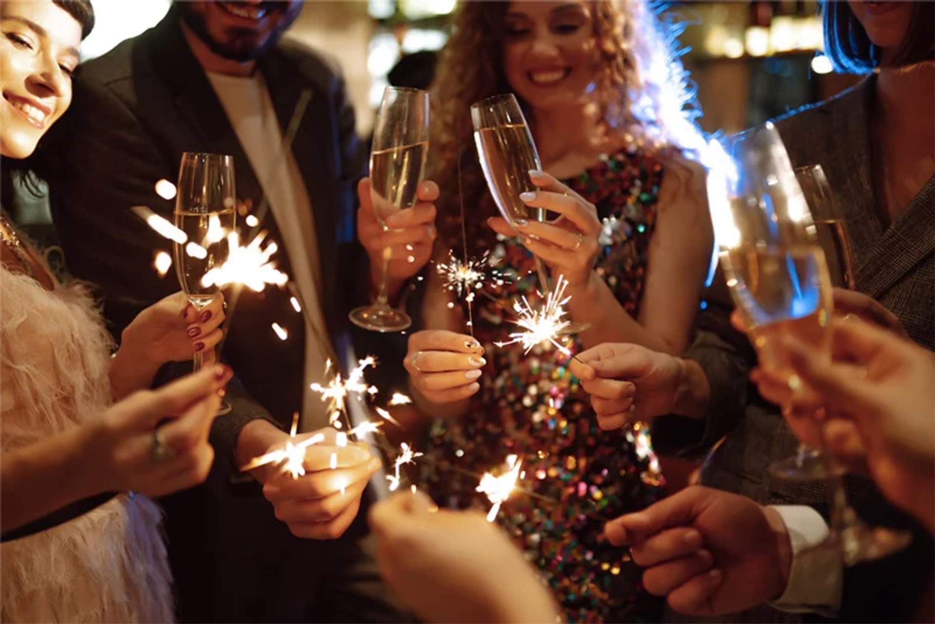 Un grupo de personas celebrando con bengalas y copas de champán, sonriendo y disfrutando de la atmósfera festiva. La toma de cerca captura el ambiente alegre y las luces brillantes.