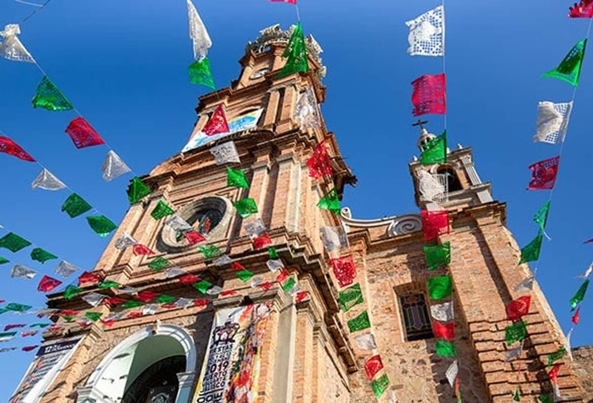 Primer plano de la Iglesia de Nuestra Señora de Guadalupe en Puerto Vallarta con banderines festivos.