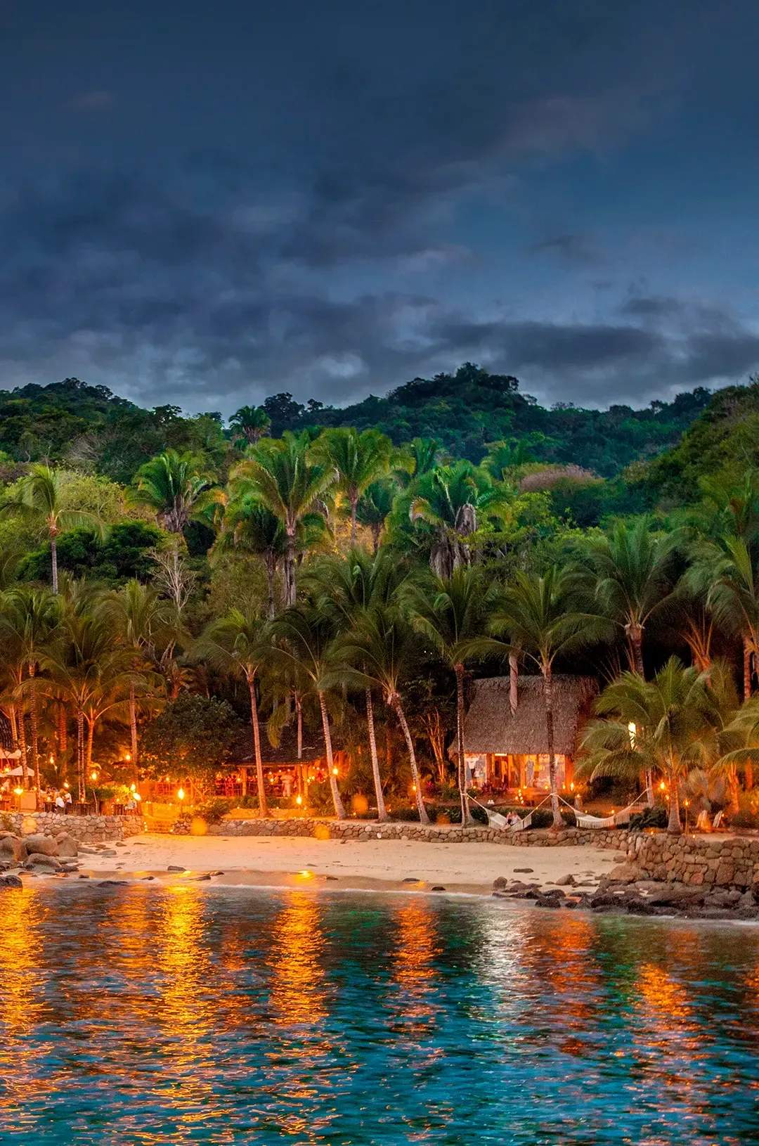 Playa iluminada con antorchas en Ritmos de la Noche, una cala escondida al atardecer en Puerto Vallarta.