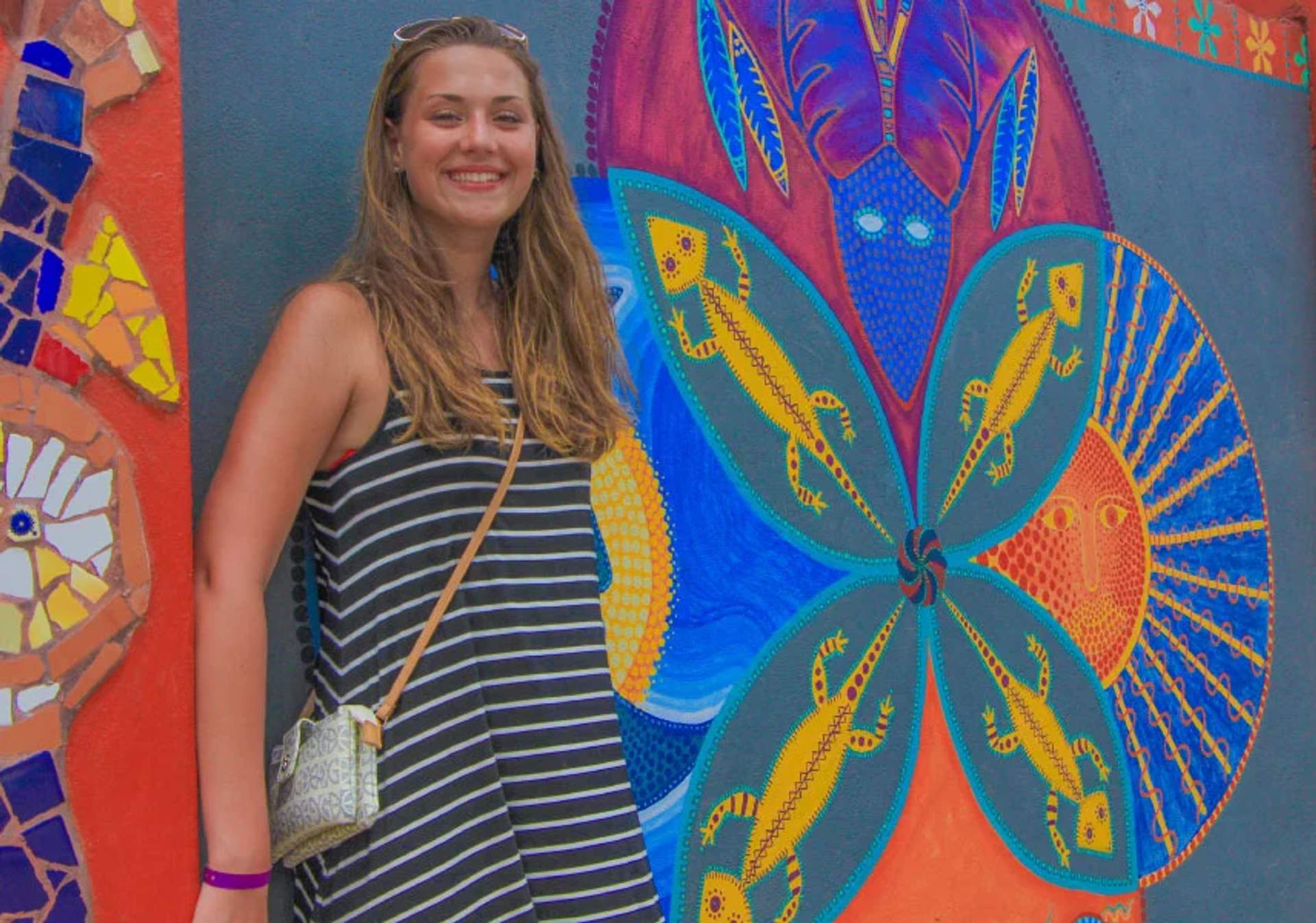 Smiling woman standing in front of a colorful mural with lizard and abstract designs in San Pancho, Mexico.