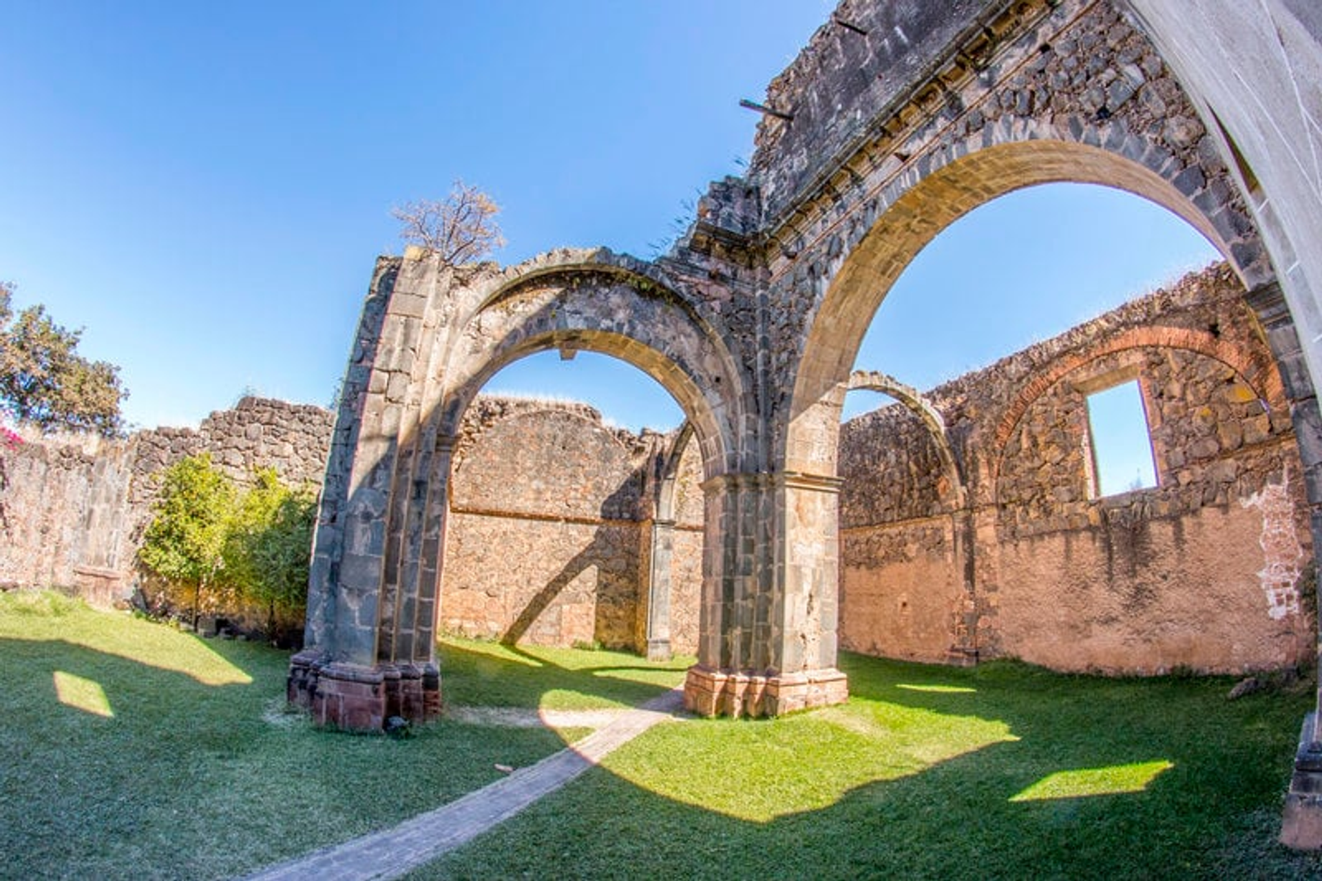 Ruinas de una antigua capilla con arcos de piedra y ventanas abiertas bajo un cielo azul claro.