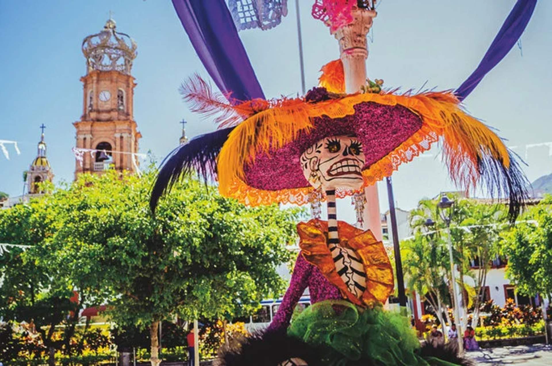 Colorful Day of the Dead Catrina decoration in Puerto Vallarta with a church tower and trees in the background.