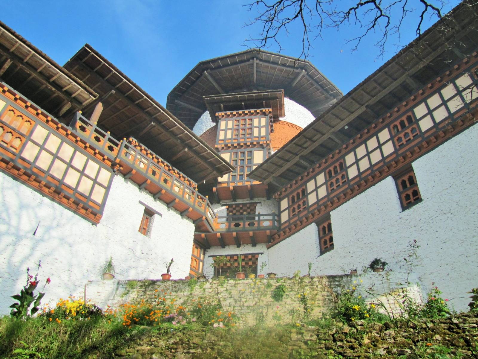 The round Ta Dzong tower between its two wings, above a terrace of flowers in Trongsa