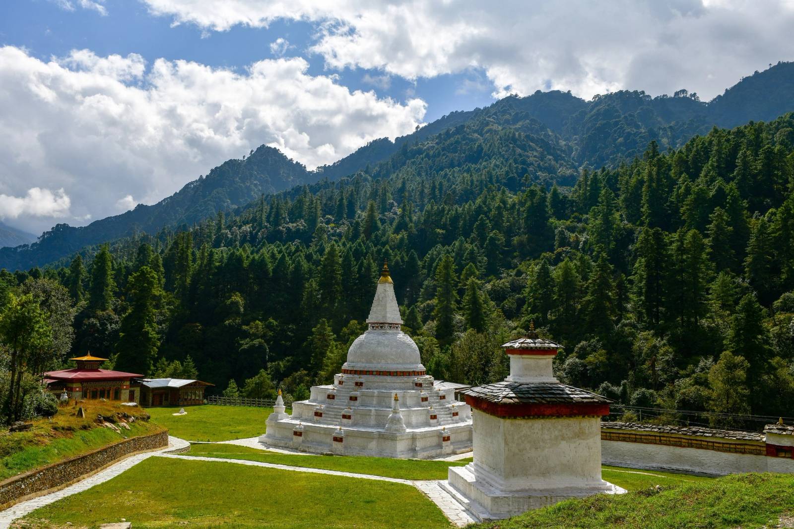 The white Chendebji Chorten on a lawn below forested hills, a smaller chorten in front