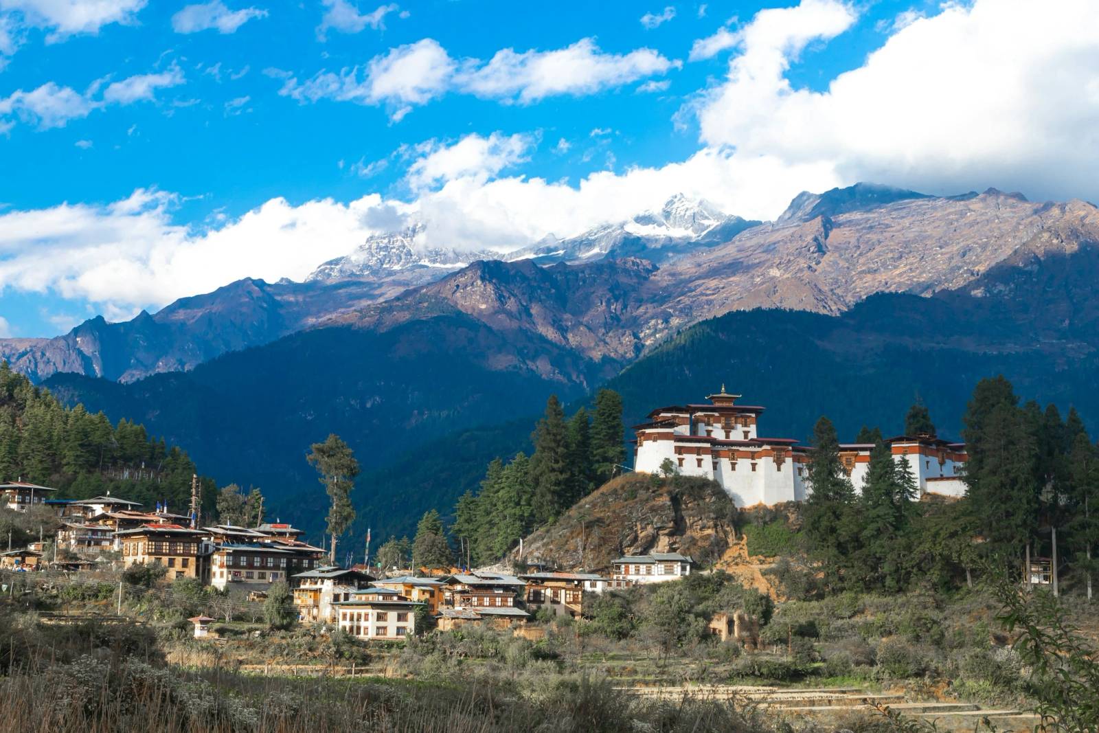 A dzong on a hillside with snow-capped mountains behind