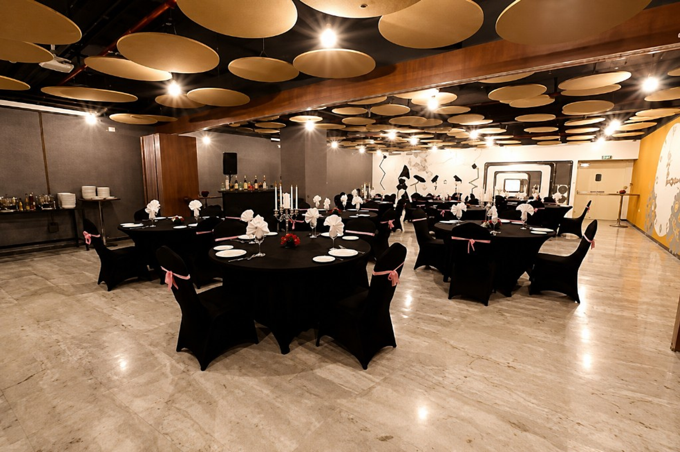 Smaaash banquet hall with black table settings, pink chair ribbons, and suspended circular ceiling panels