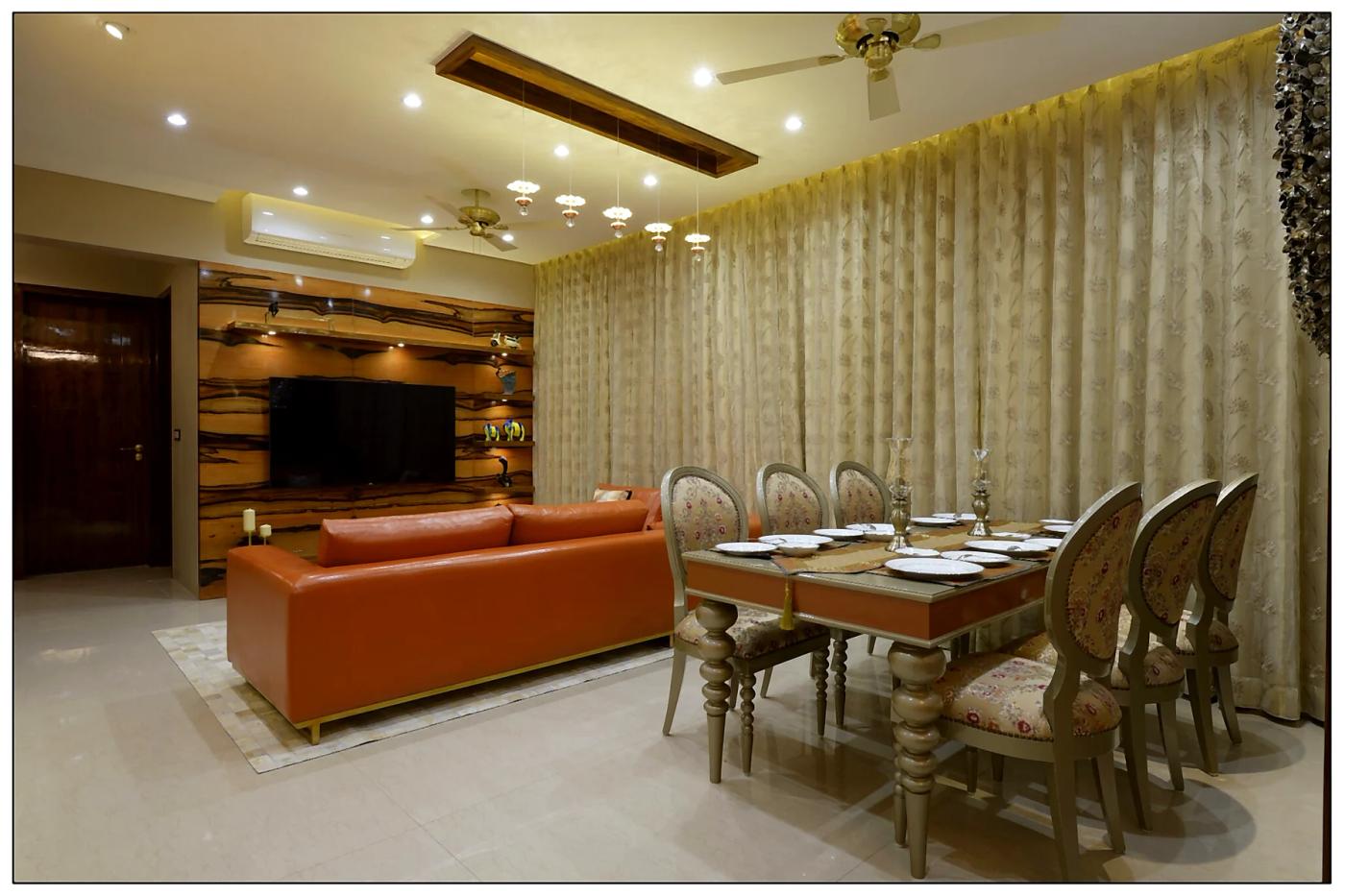 Open living and dining with orange leather sofa, wood media wall, and floral dining chairs