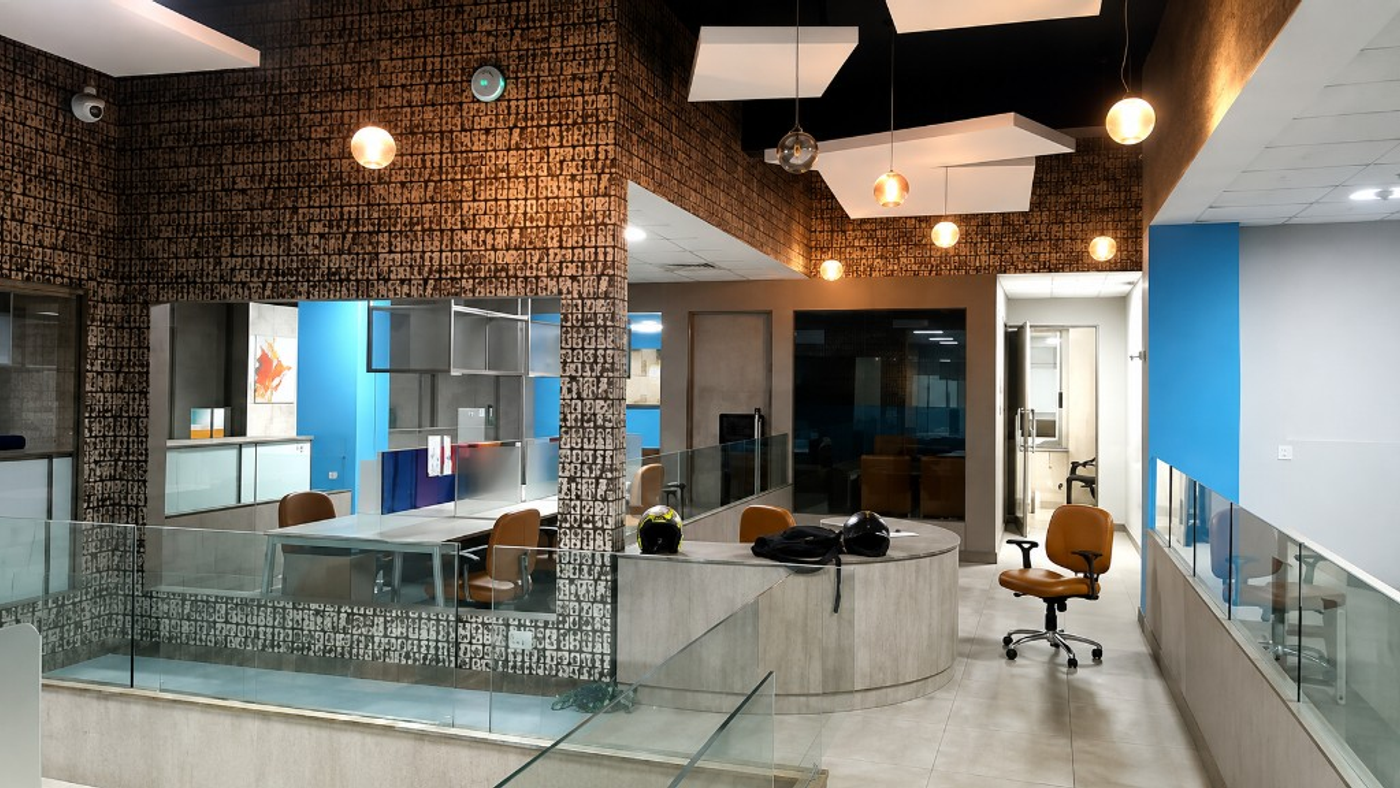 MBD Office open-plan interior with glass railings, blue accent walls, tan chairs, and globe pendants