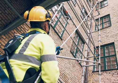 En byggarbetare utrustad med fallskydd vid en ställning, vilket illustrerar Ramirents fokus på säkerhet och kvalitet i samarbetet med våra leverantörer.