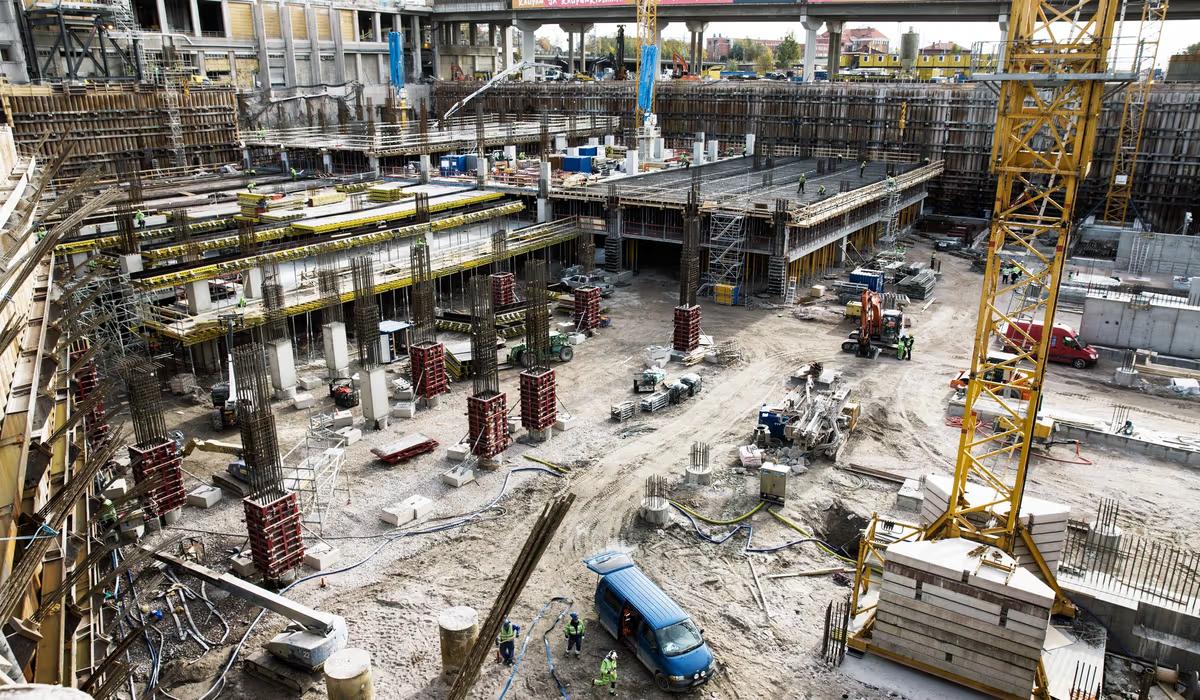 Stor byggarbetsplats med betongstomme, kran och byggutrustning i arbete.