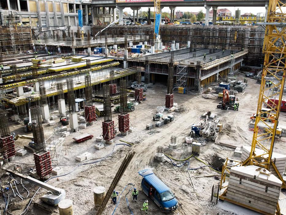 Stor byggarbetsplats med betongstomme, kran och byggutrustning i arbete.