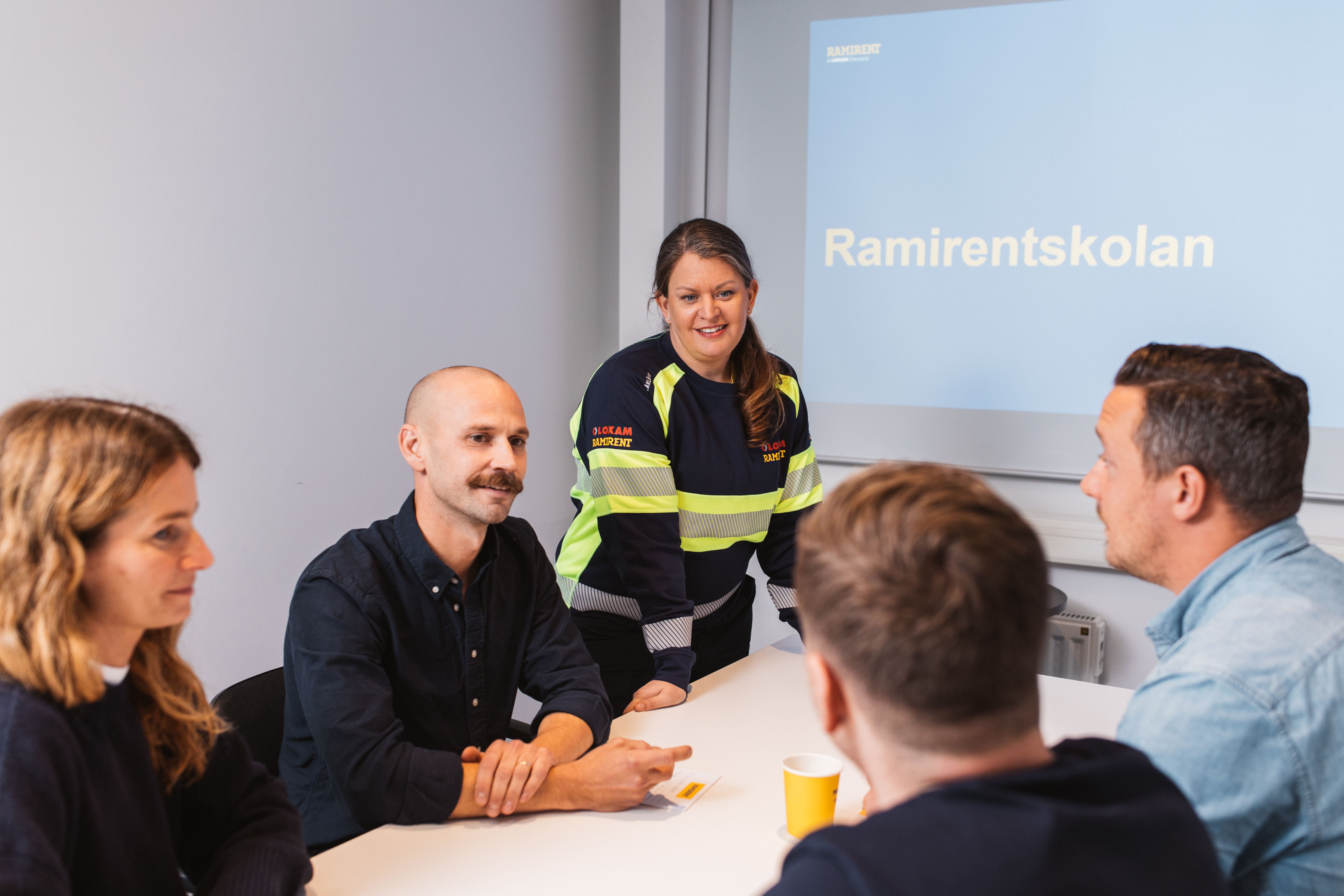 Ramirentskolan: Instruktör i varselkläder leder en lärarledd kurs i säkerhet med kursdeltagare i klassrum. Ta del av Ramirents utbildningar.