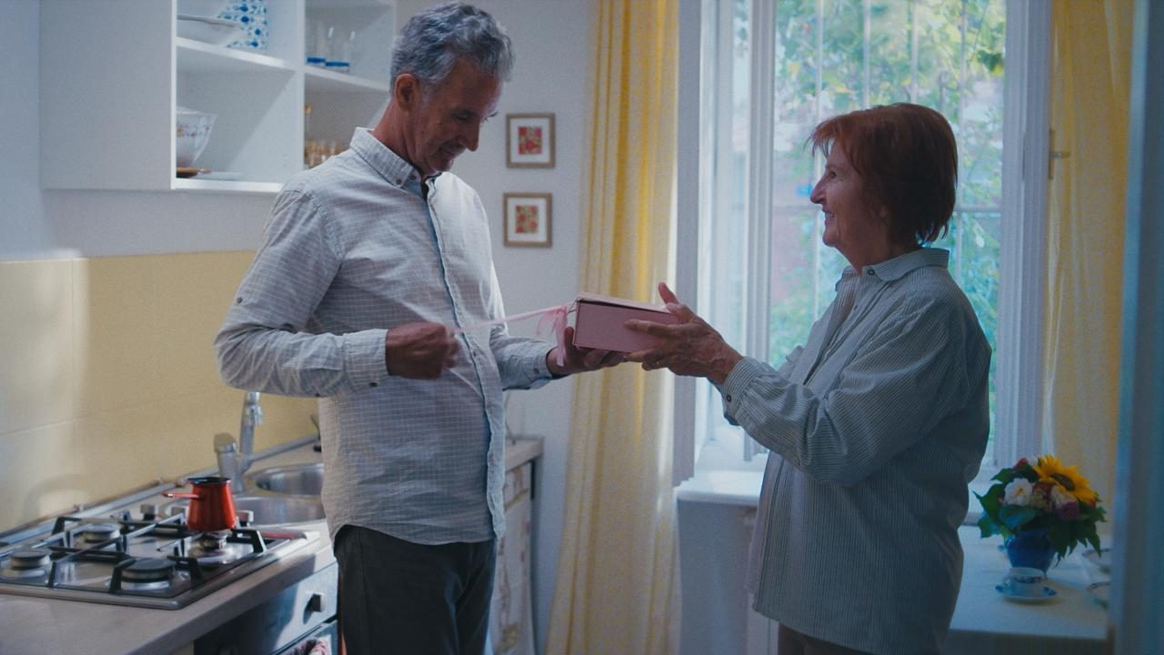 Ivica hands Zdenka a present in the kitchen