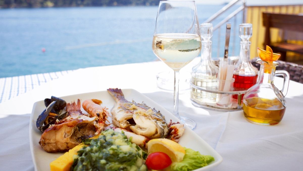 A picture of a meal with grilled fish and wine in an ocean view