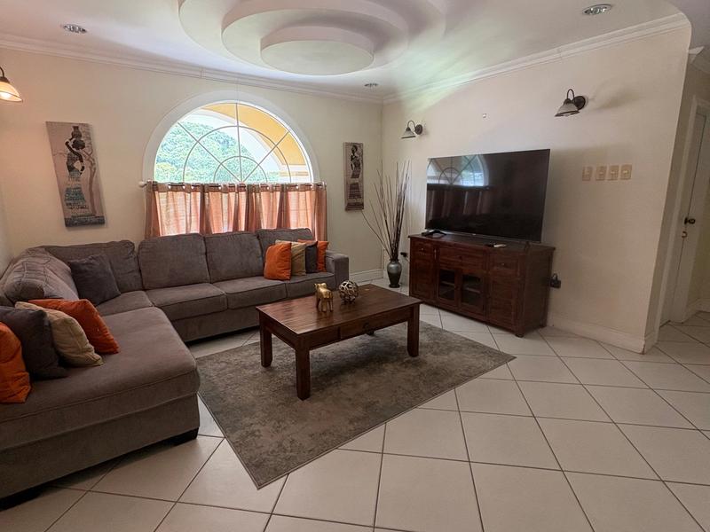 Comfortable living room with a large brown sectional sofa, coffee table, Smart TV and an arched window overlooking the greenery outside.