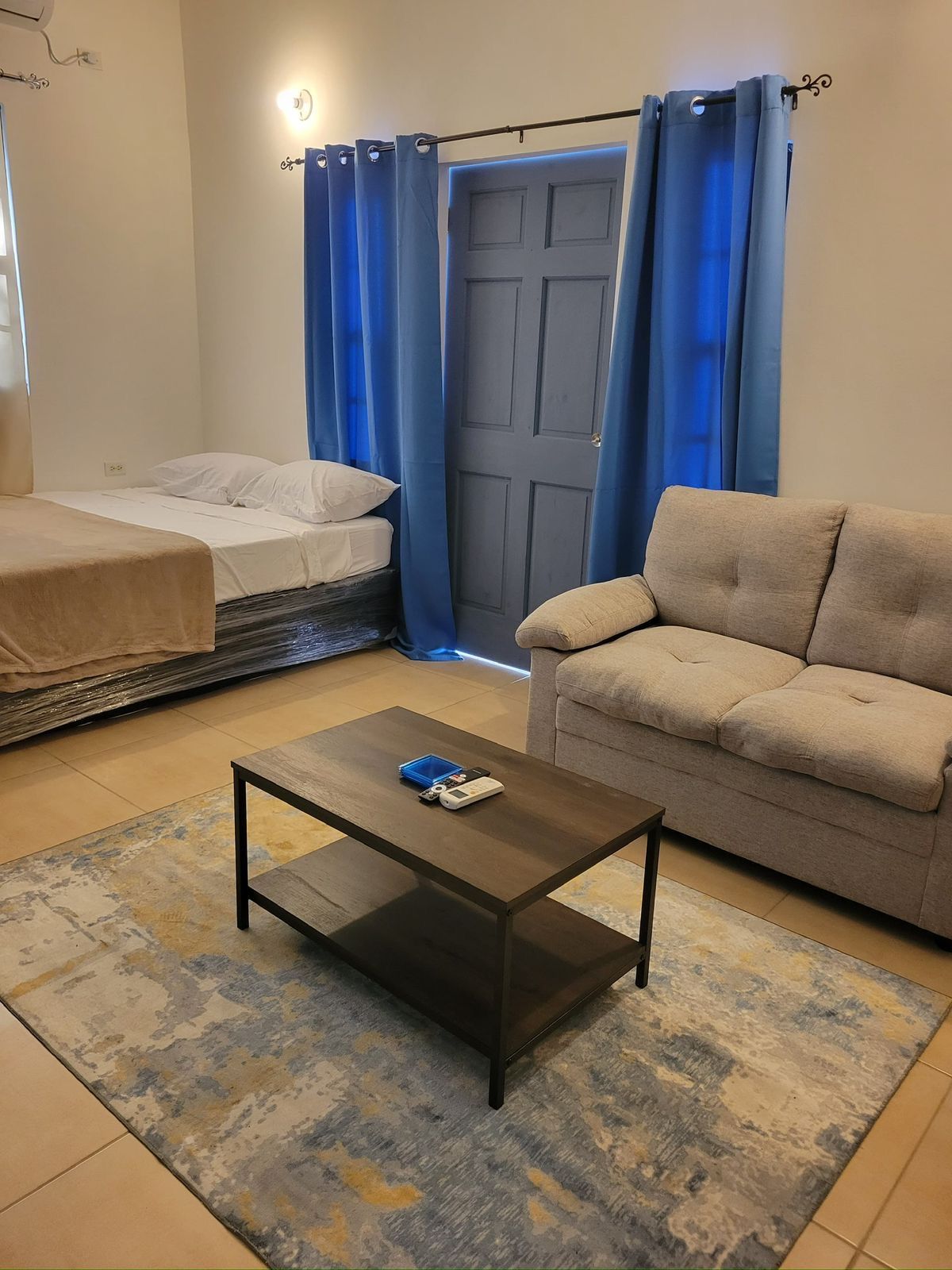 Room with a double bed, two-seat sofa and blue curtains