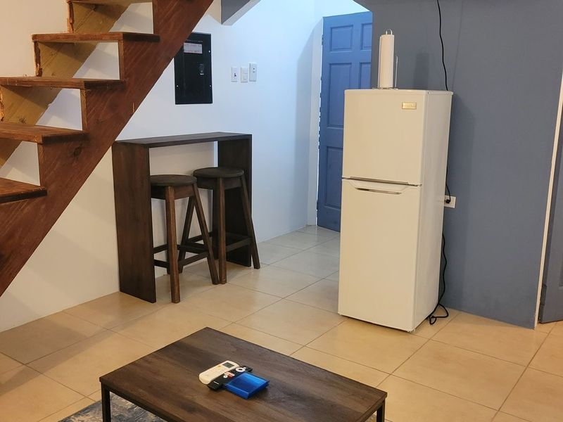 Breakfast bar with two stools beneath a wooden staircase, beside a fridge and wall-mounted television