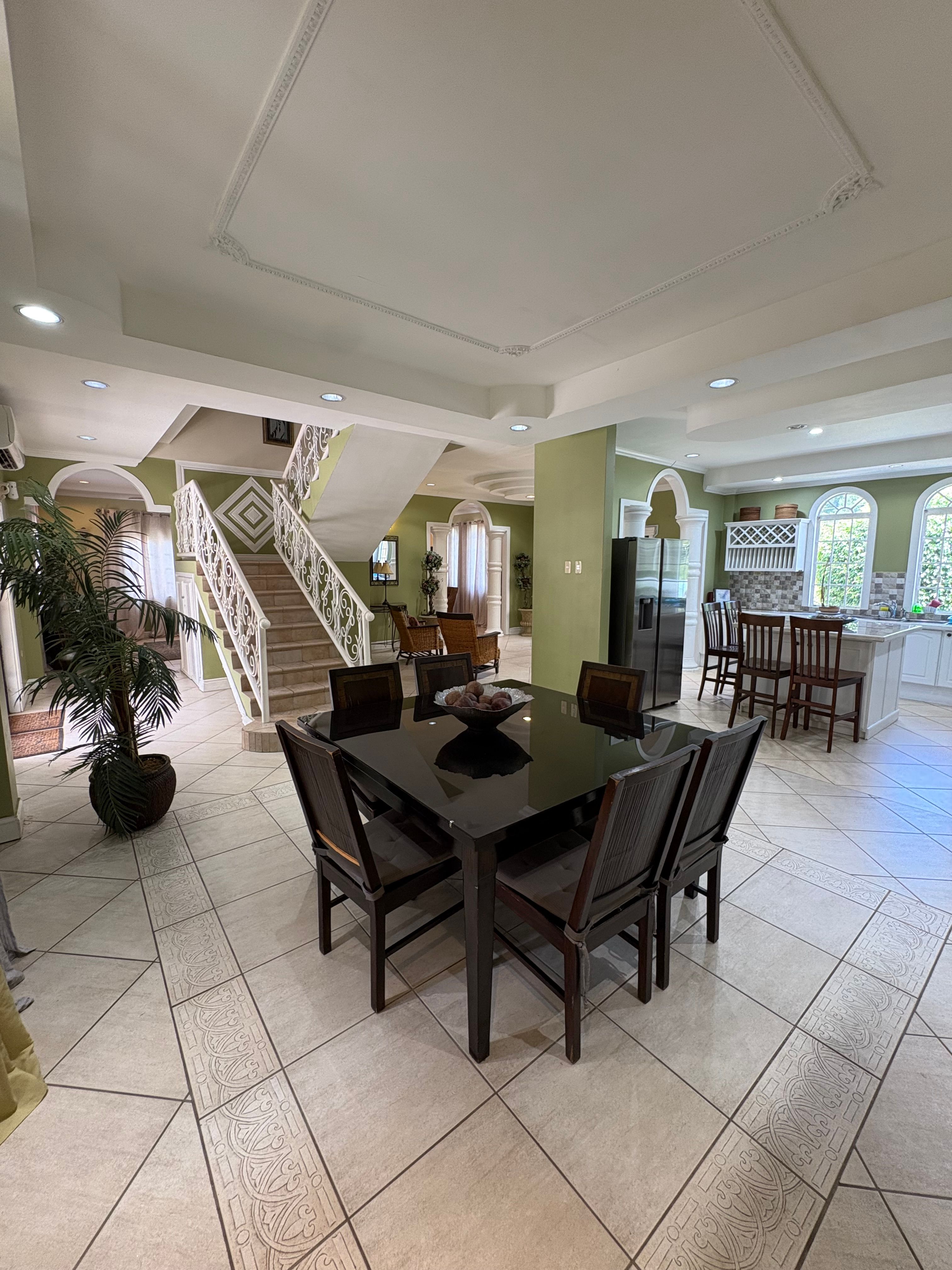 Open-plan dining area featuring a dark wooden dining table, decorative staircase and direct access to the fully equipped kitchen.