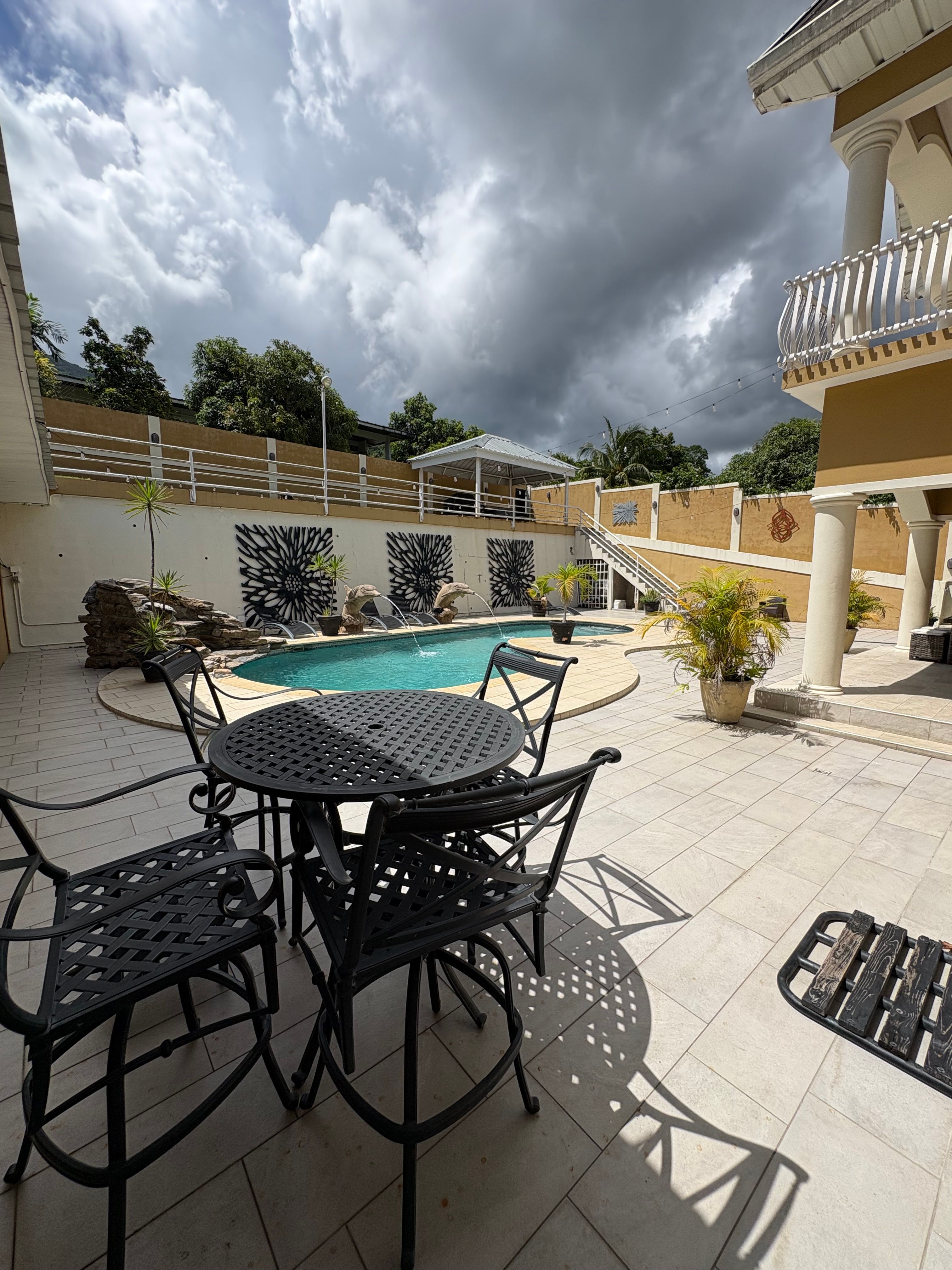 Outdoor pool area featuring a swimming pool, patio dining furniture, lounge chairs and a spacious courtyard surrounded by the villa’s exterior.