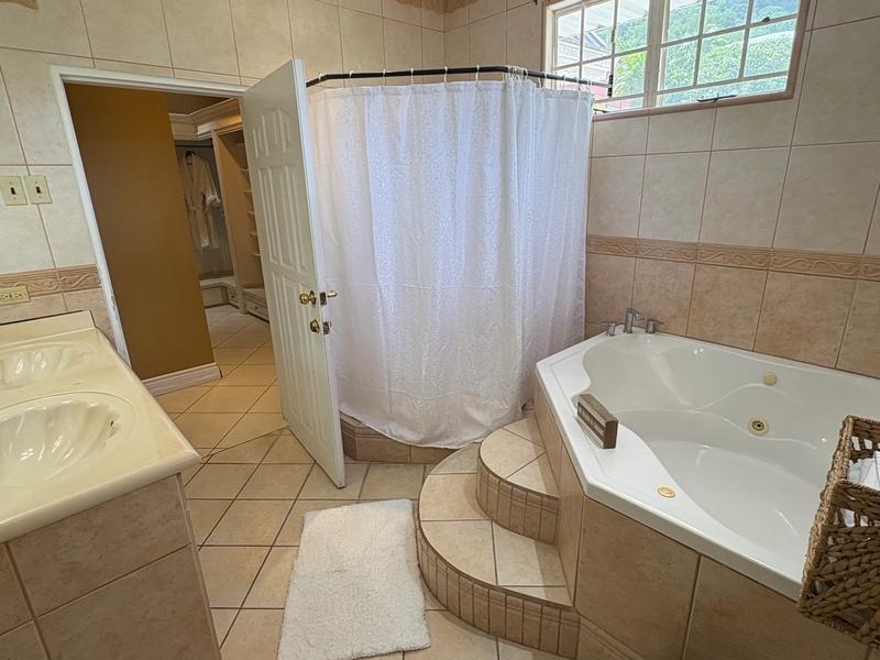 Spacious tiled bathroom featuring a corner jacuzzi bathtub, separate shower, vanity and a window overlooking the surrounding greenery.