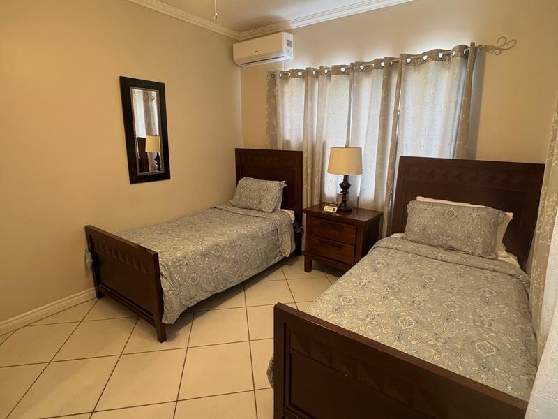 Air-conditioned guest bedroom with two single beds, wooden furniture, matching bedding and natural light through curtained windows.