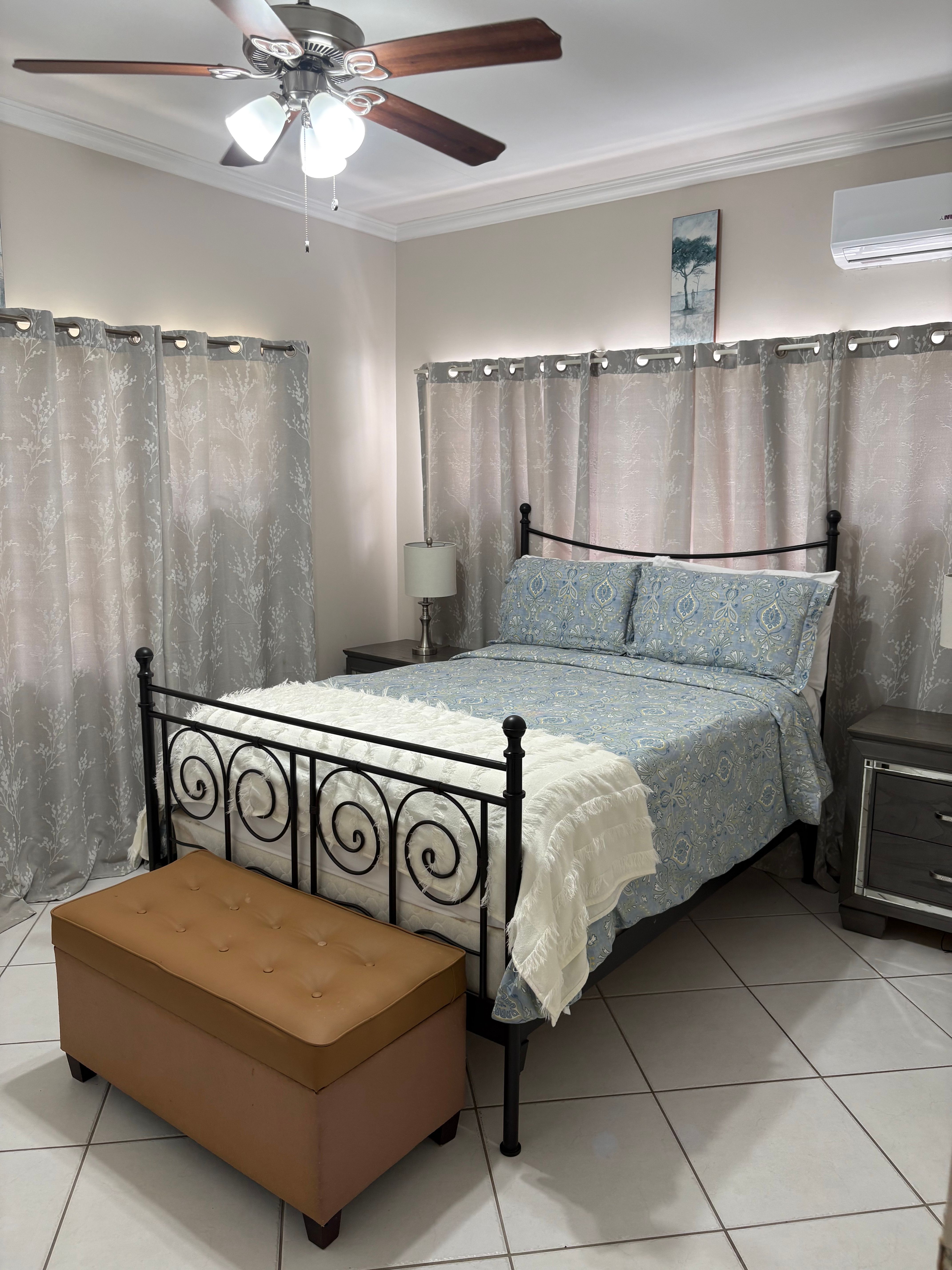 Comfortable bedroom featuring a queen sized bed with a decorative metal frame, bedside tables, air conditioning and a ceiling fan.